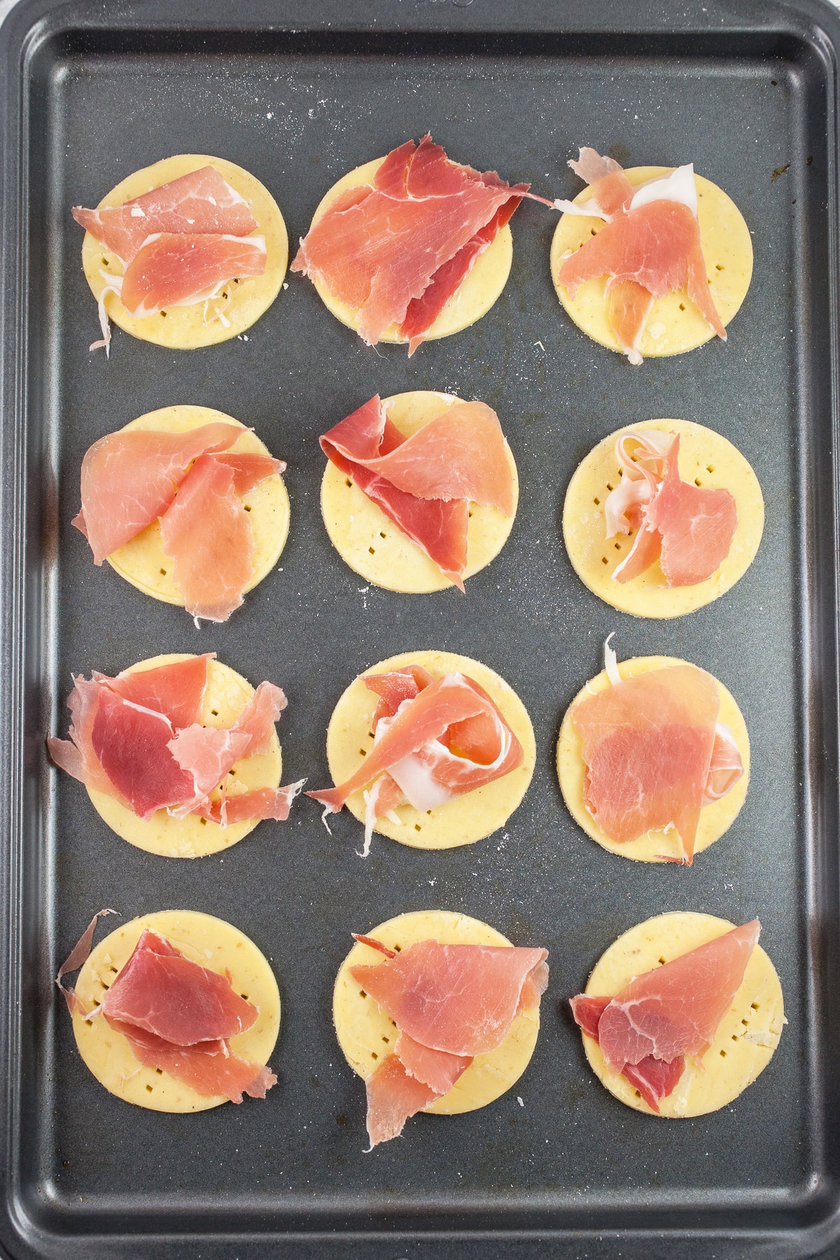 Puff pastry rounds with prosciutto on baking sheet.