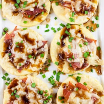 Gruyere prosciutto tartlets with balsamic glaze and minced chives on white platter.