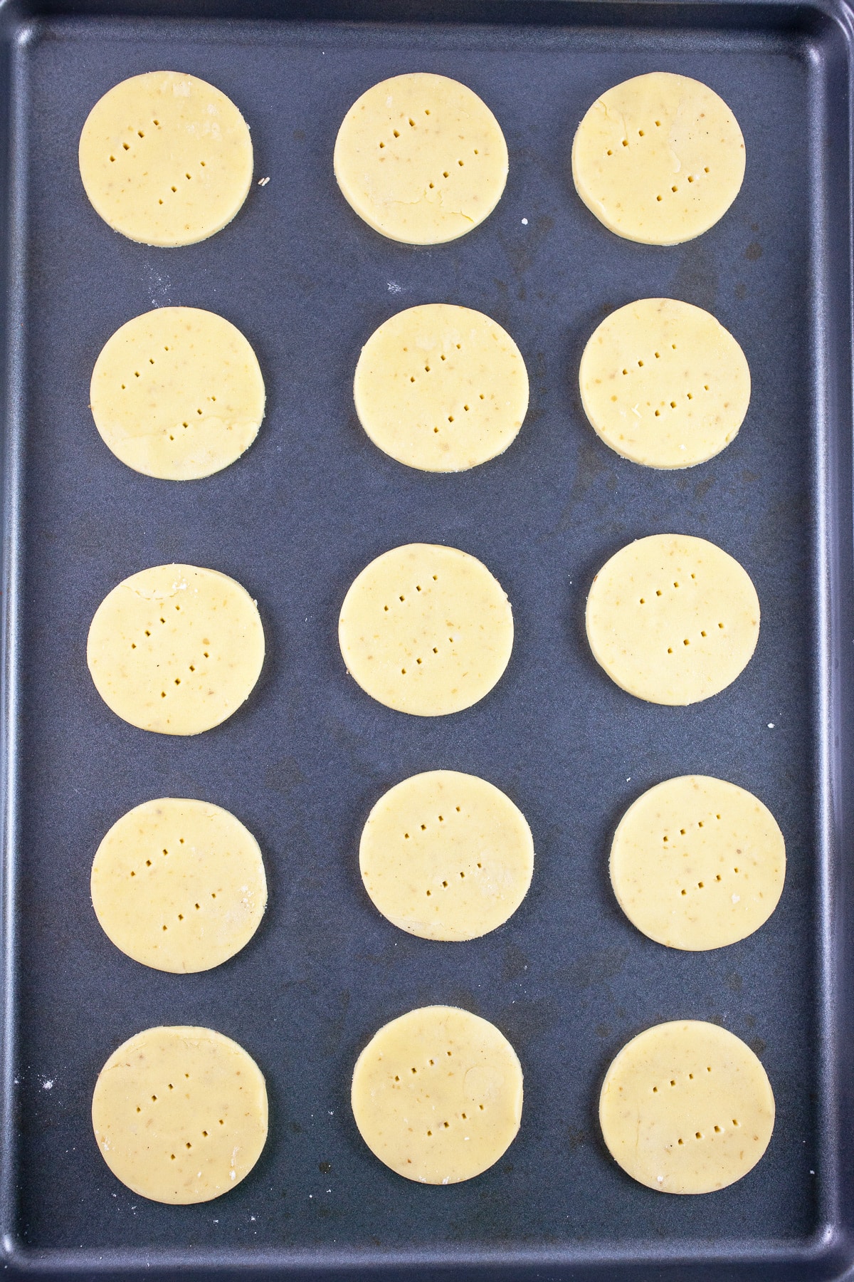 Puff pastry rounds pierced with fork on baking sheet.
