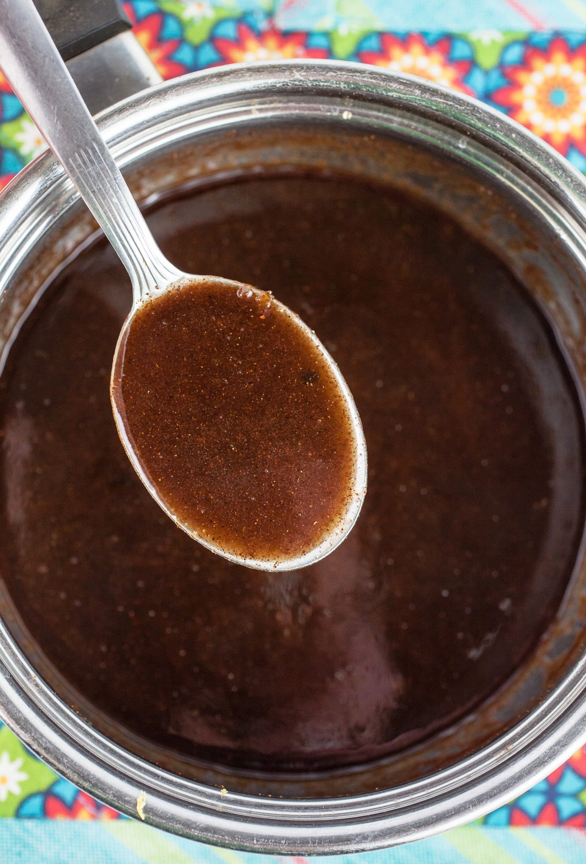 Spoonful of spiced maple syrup glaze lifted from sauce pan on potholder.