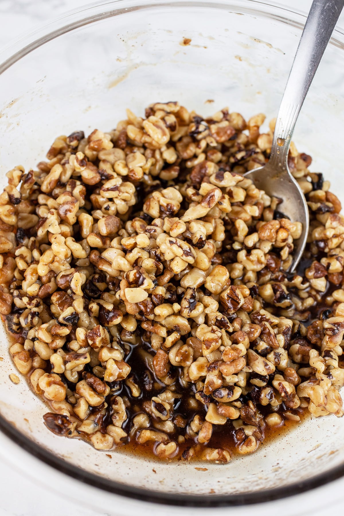 Maple syrup walnut mixture in large glass bowl with spoon.