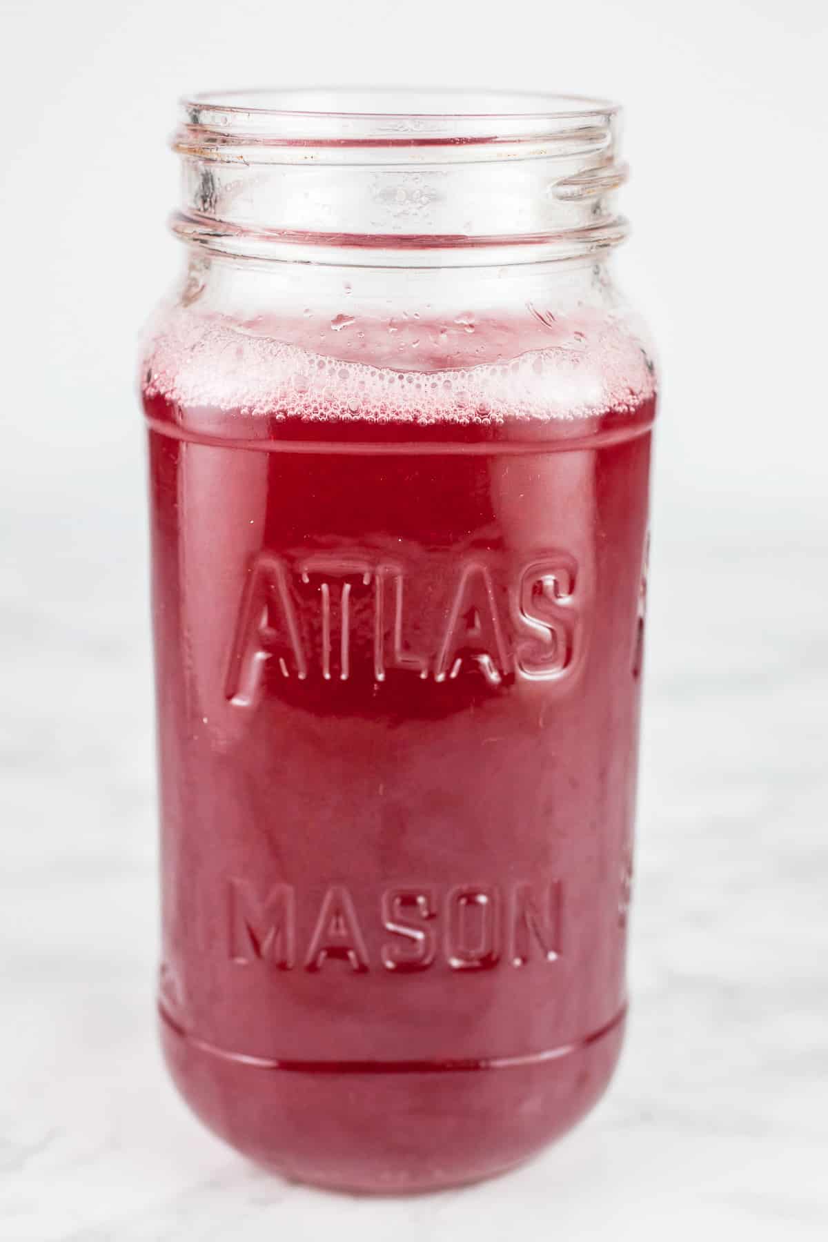 Raspberry cordial syrup in mason jar on white surface.