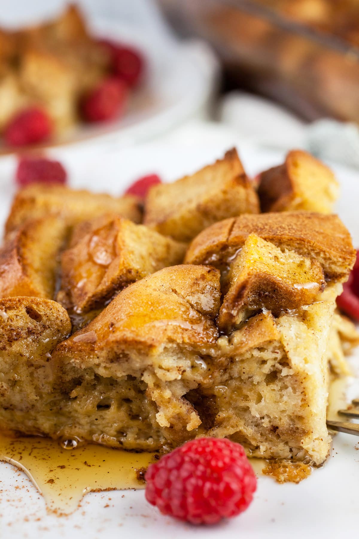 Gluten free French toast casserole on white plates with syrup and fresh raspberries.