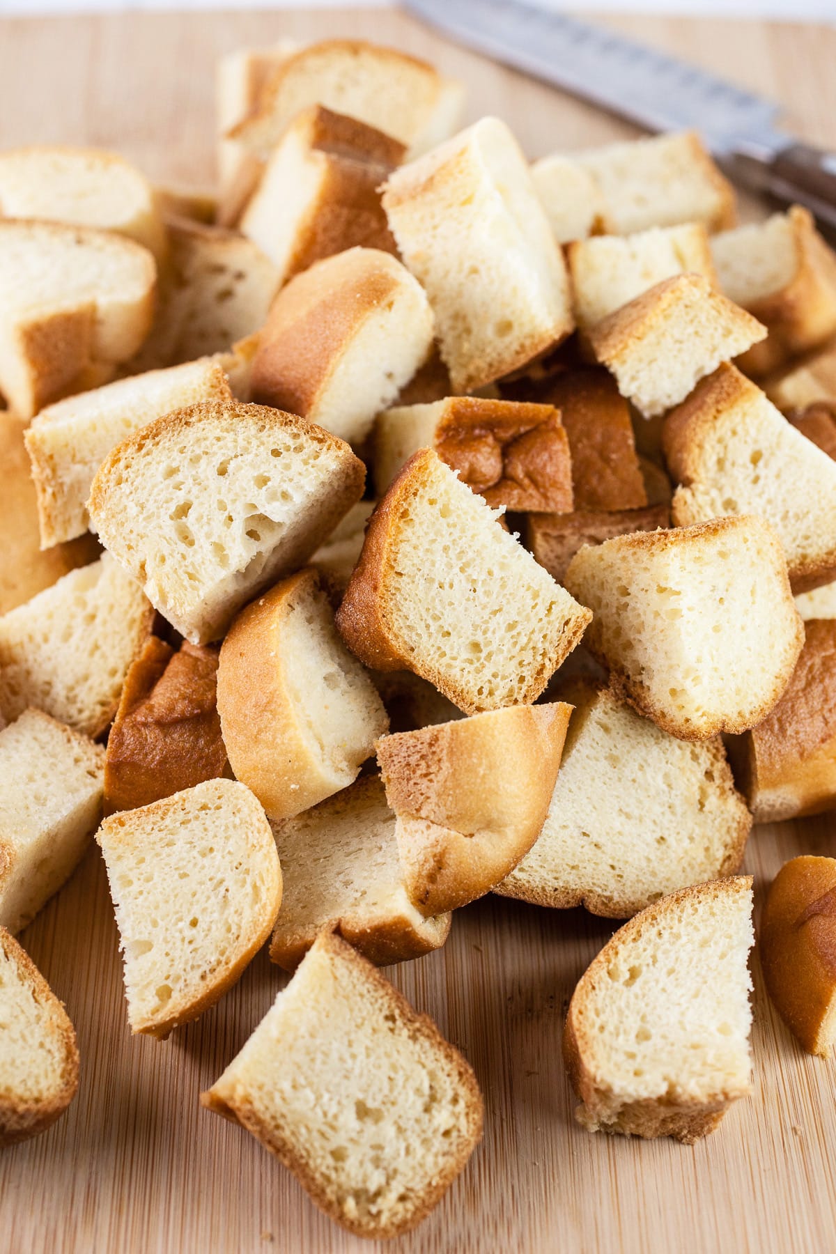 Cubed gluten free brioche buns on wooden cutting board with knife.