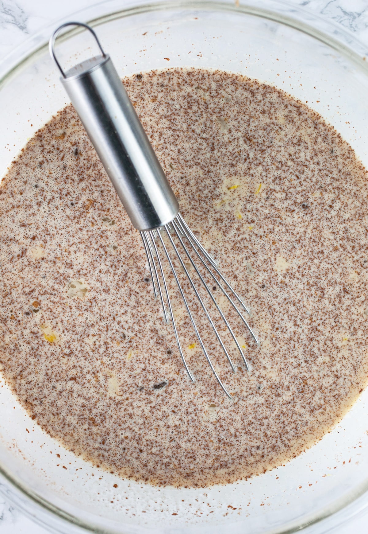 Egg custard mixture in large glass bowl with whisk.