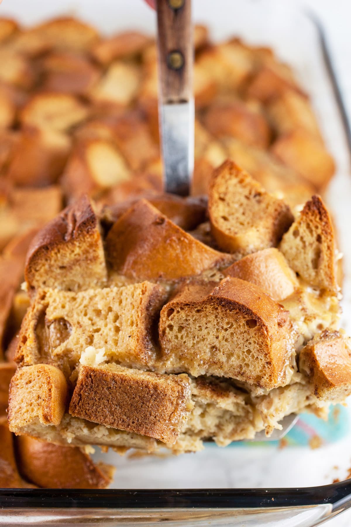 Scoop of French toast casserole lifted from glass baking dish on spatula.