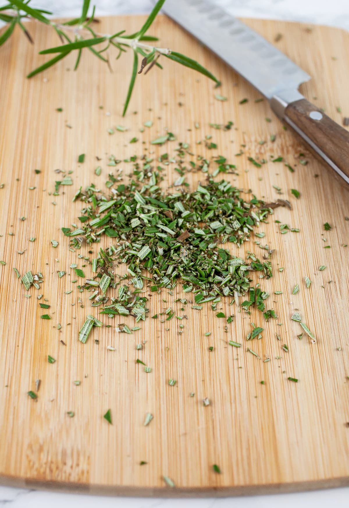 Minced fresh rosemary on wooden cutting board with knife.