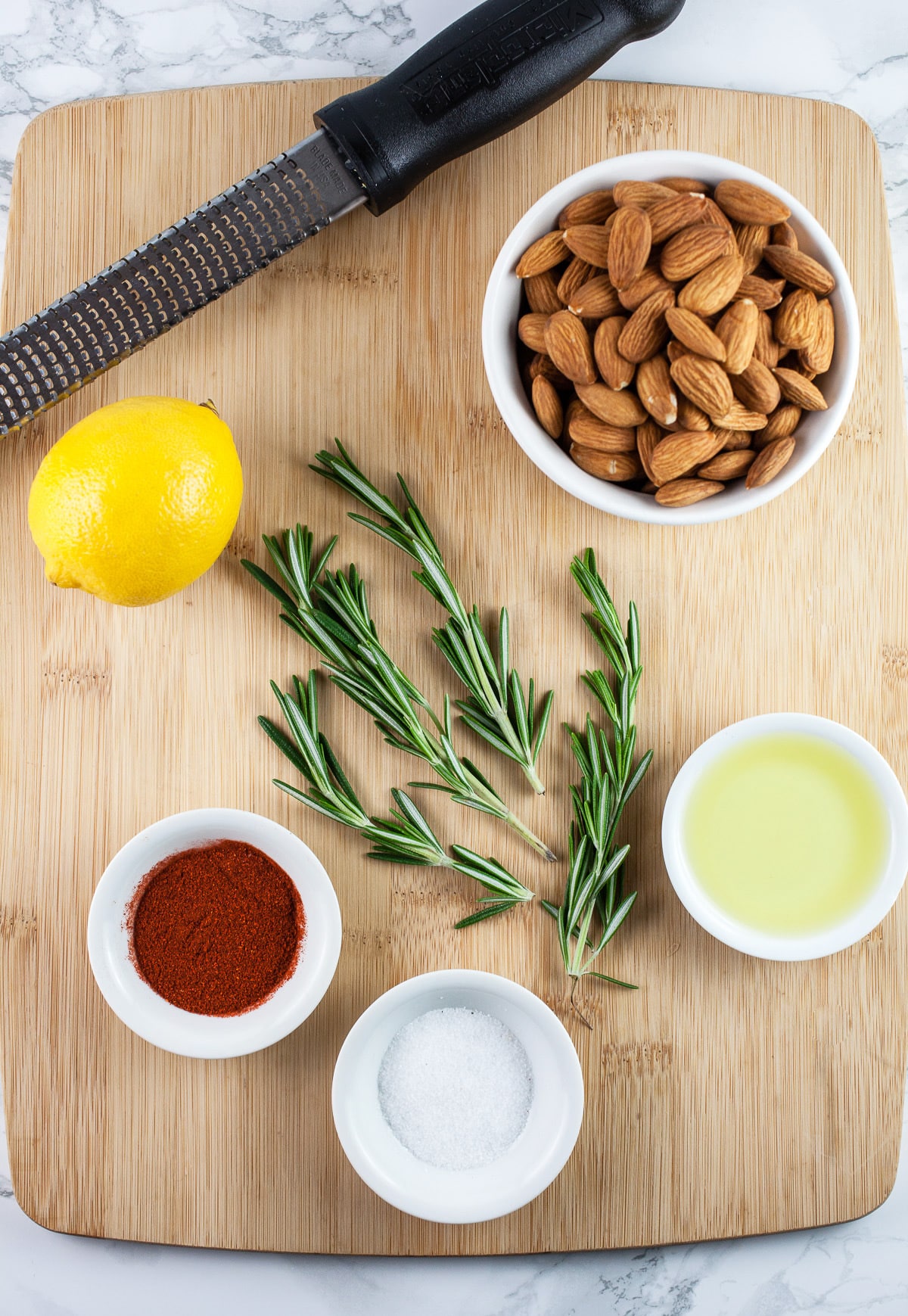 Kosher salt, smoked paprika, olive oil, fresh rosemary, lemon, almonds, and Microplane zester on wooden cutting board.