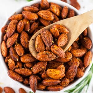 Rosemary roasted almonds in small white bowl with wooden spoon.