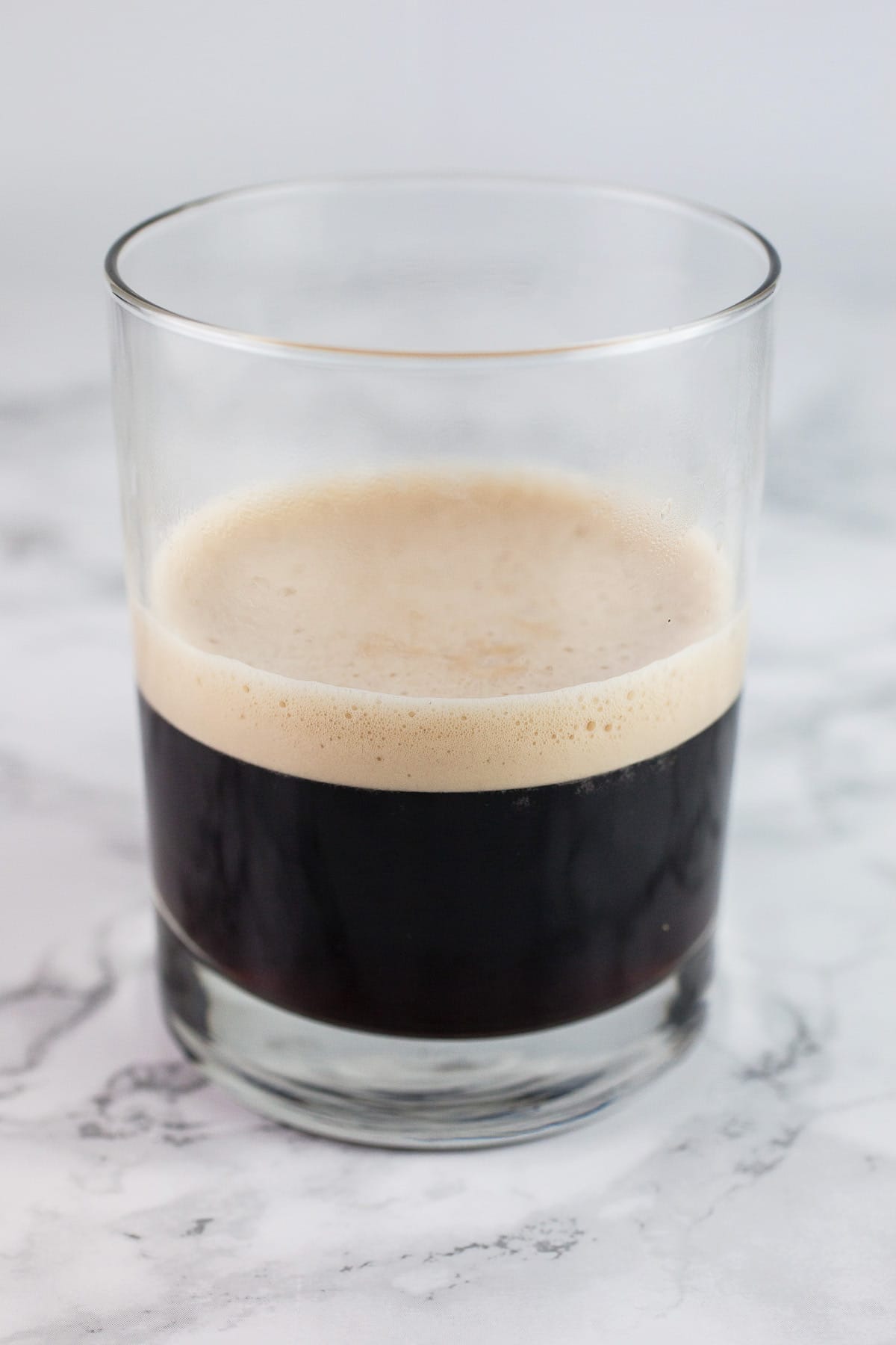 Shot of brewed espresso in glass on white surface.