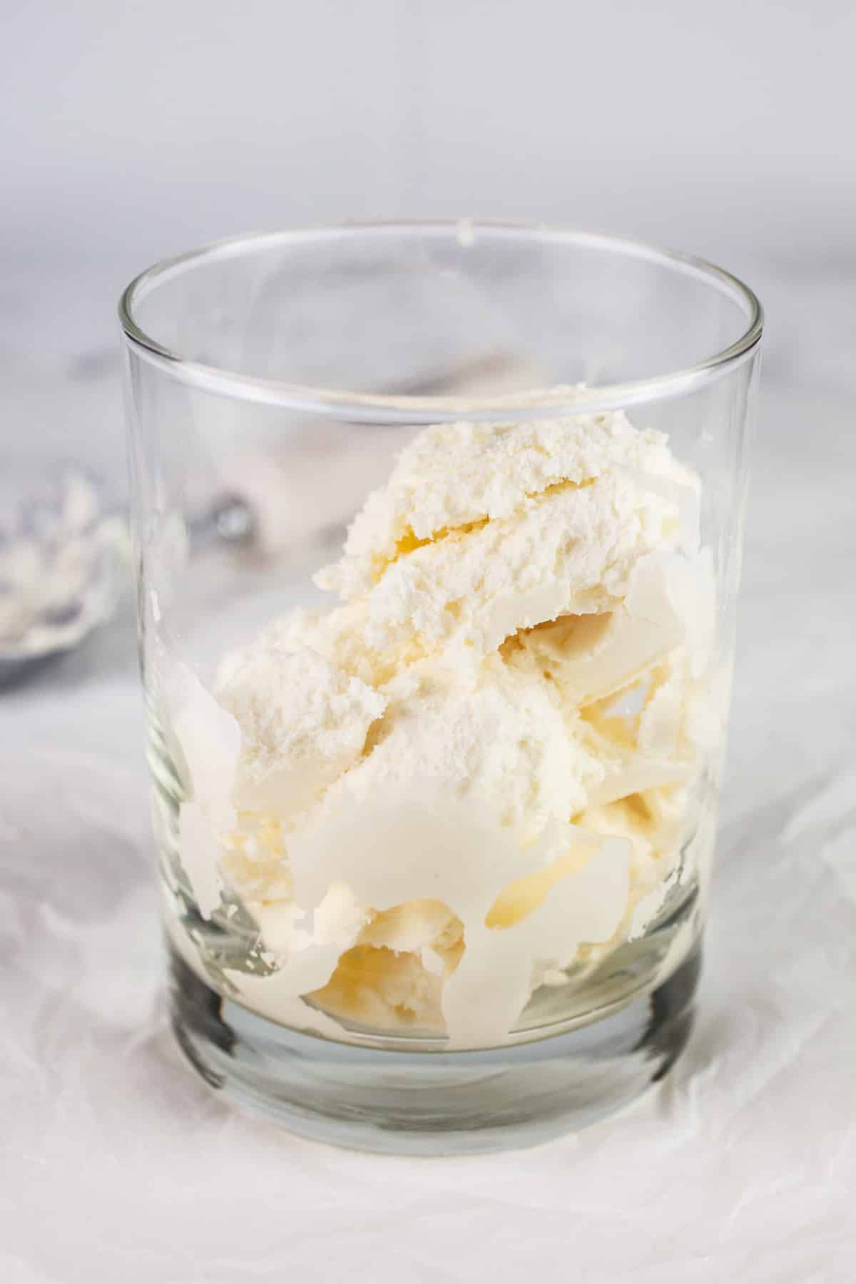 Scoops of vanilla ice cream in glass on white surface.