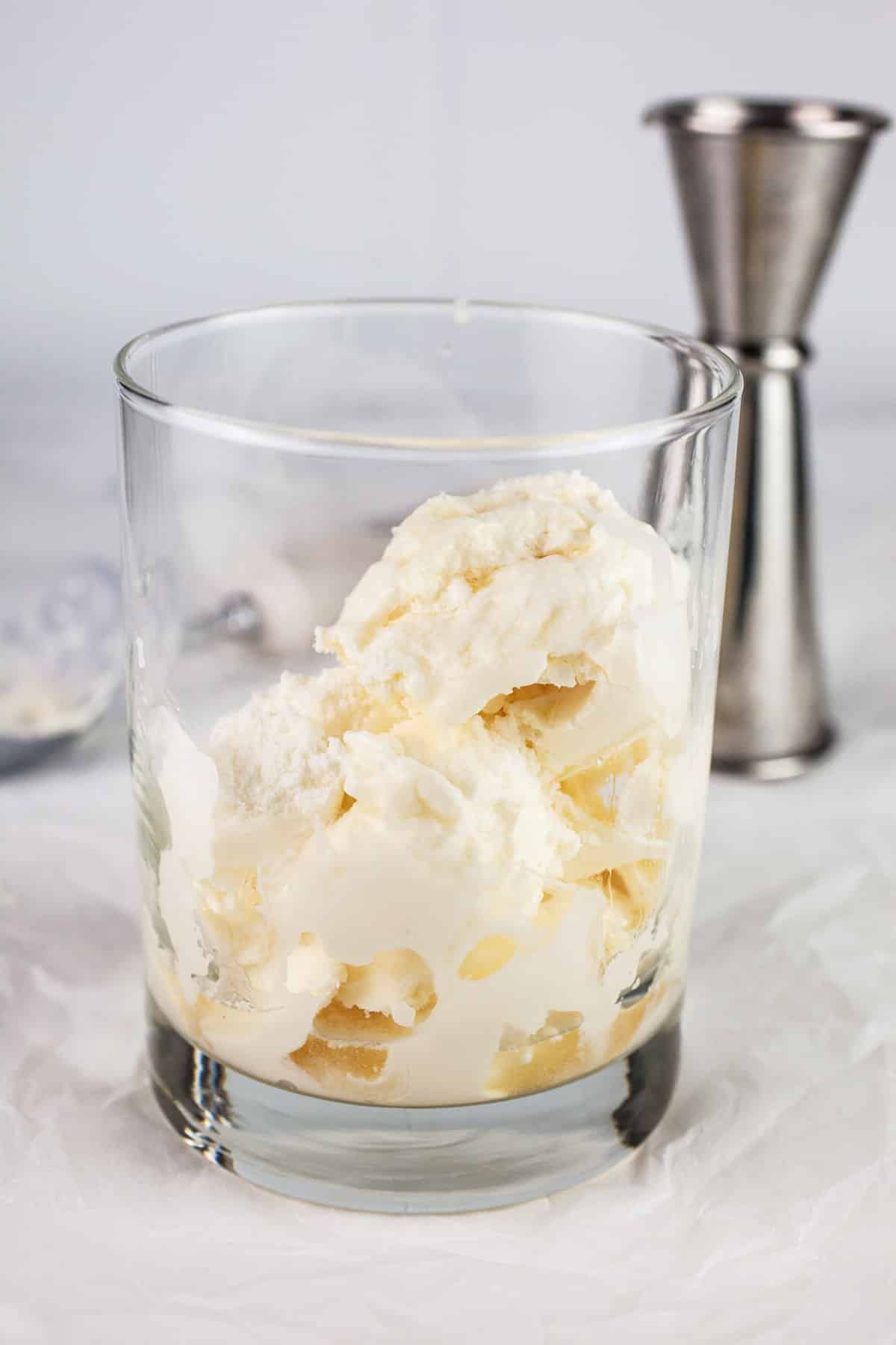 Ice cream and whiskey in glass on white surface.