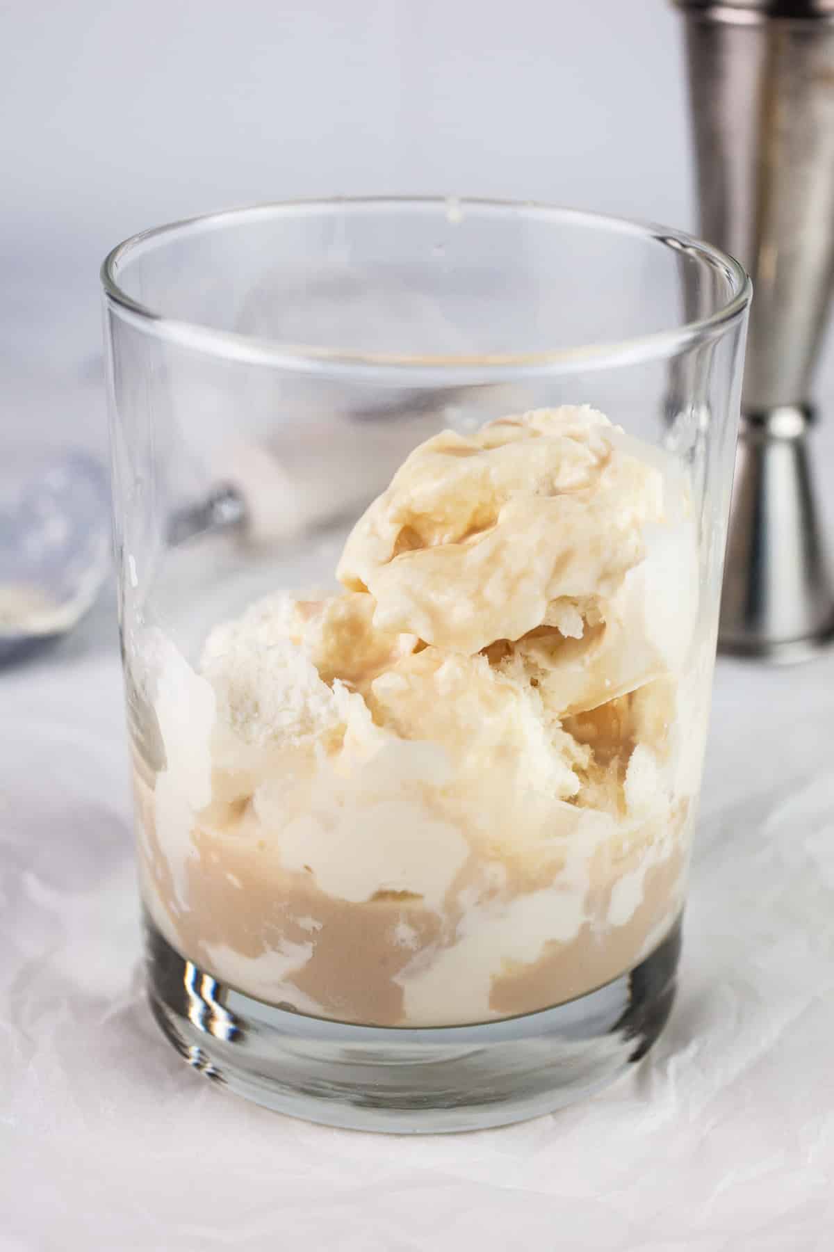 Ice cream, whiskey, and Baileys in glass on white surface.