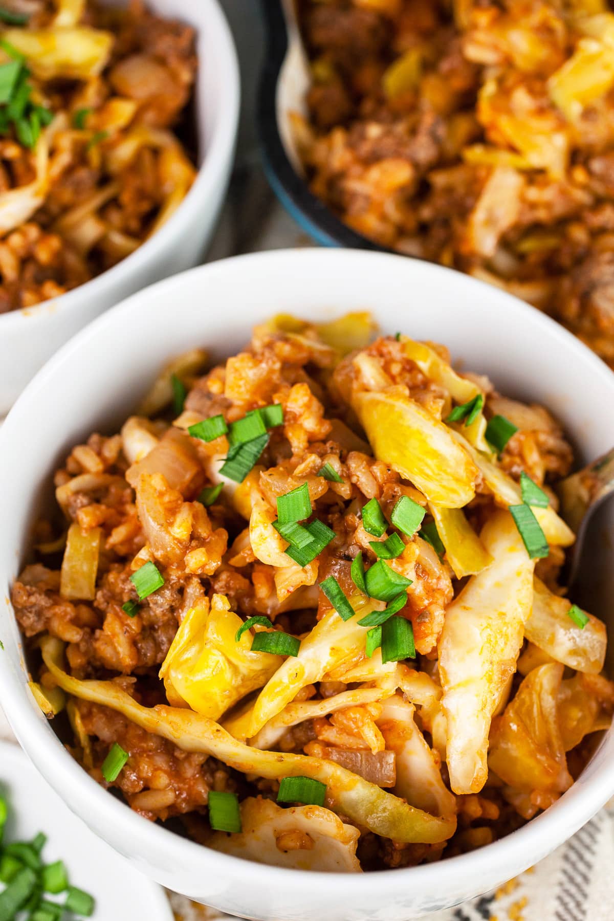 Cabbage roll in a bowl garnished with minced chives next to skillet.