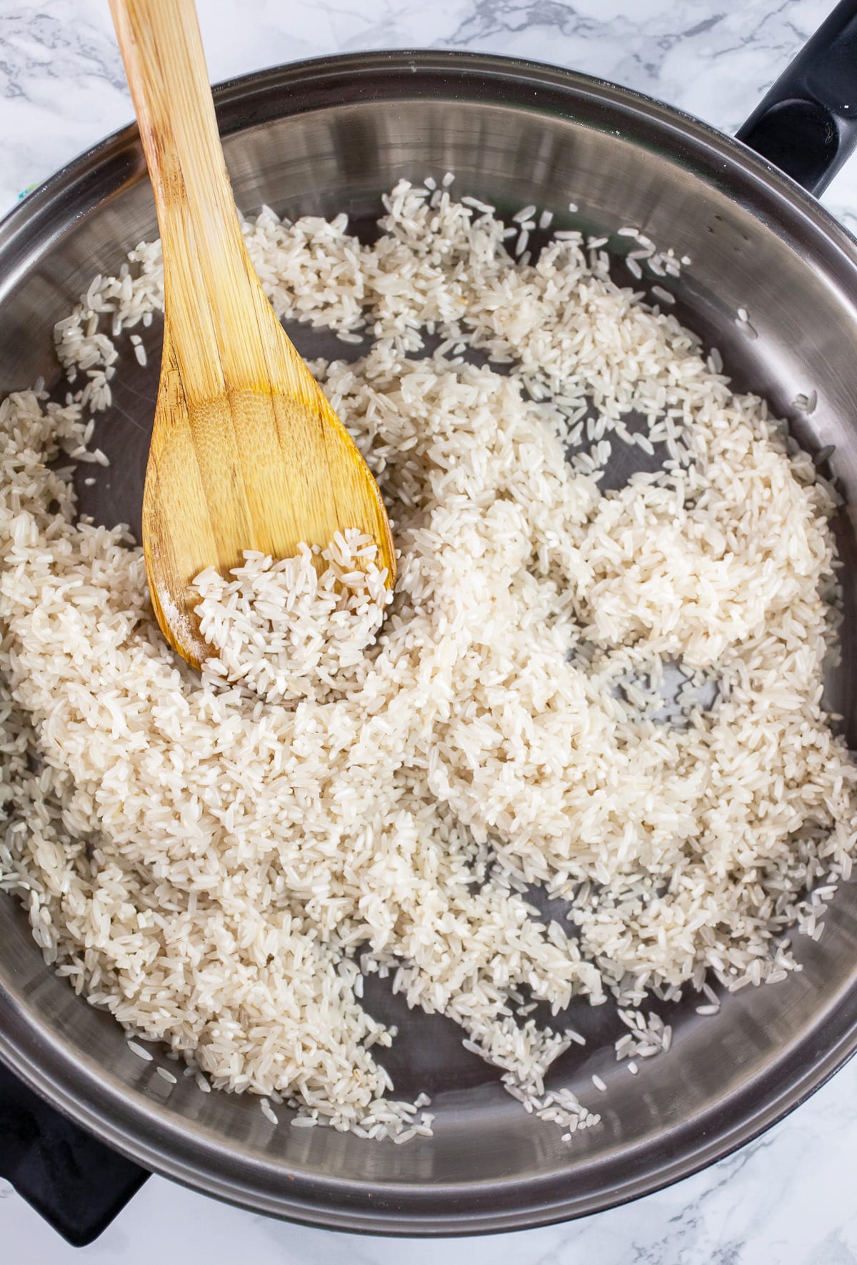 Long grain white rice sautéed in skillet with wooden spoon.