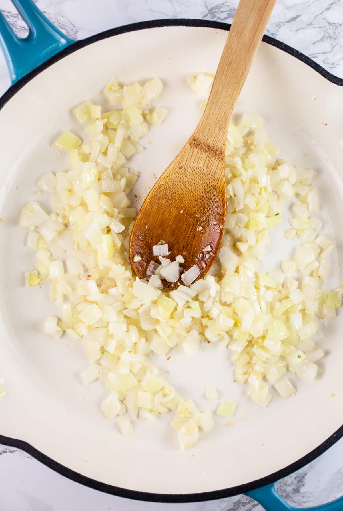 Minced garlic and onions sautéed in skillet with wooden spoon.