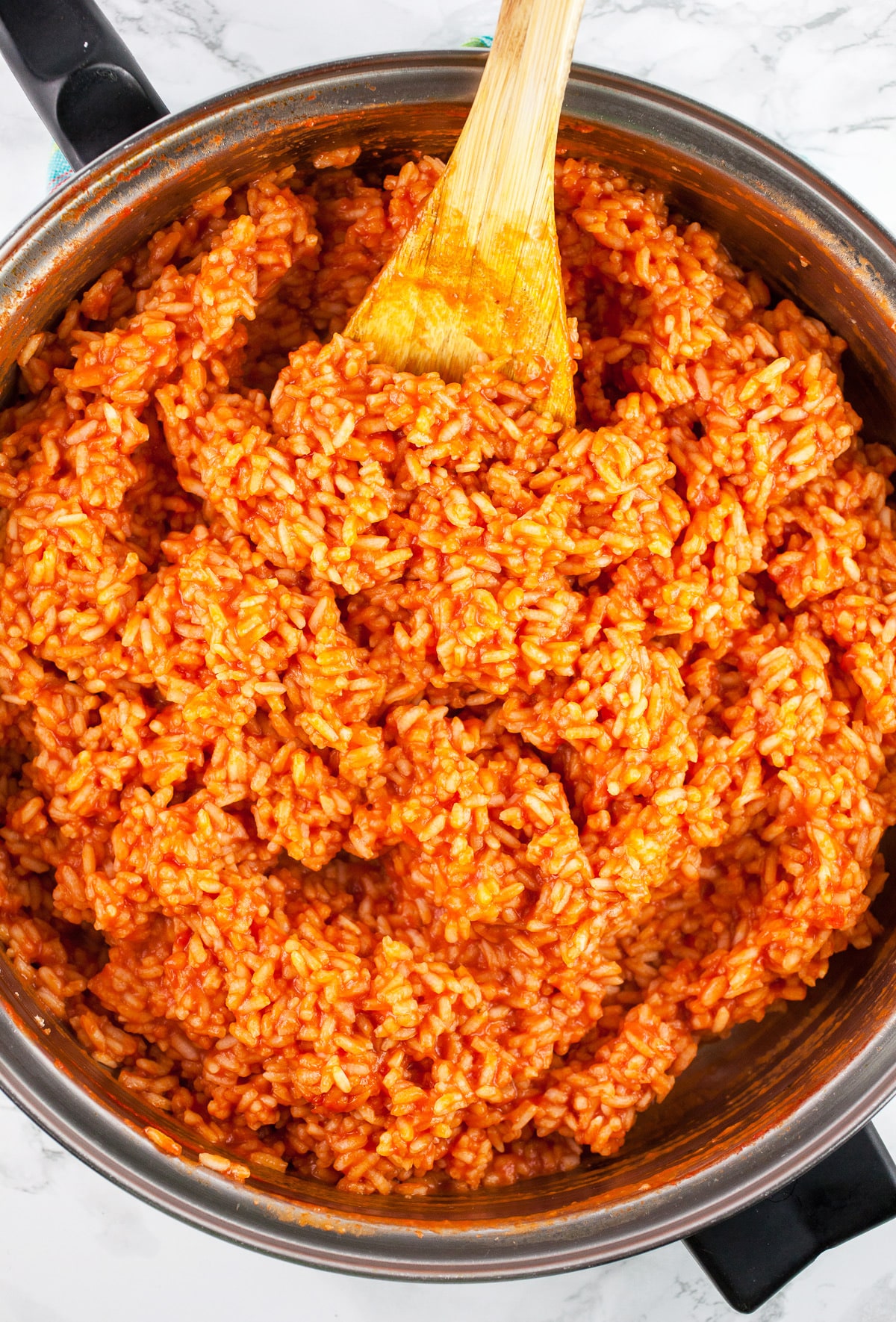 Cooked rice in tomato sauce in skillet with wooden spoon.