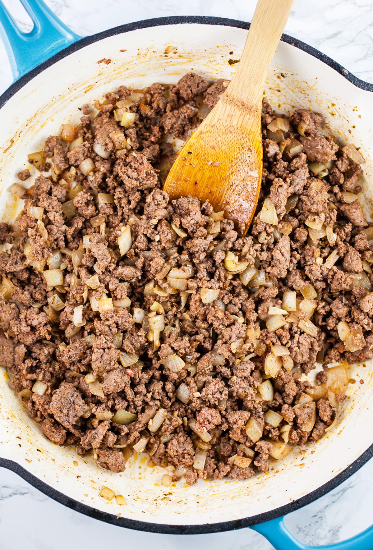 Ground beef sautéed in skillet with wooden spoon.