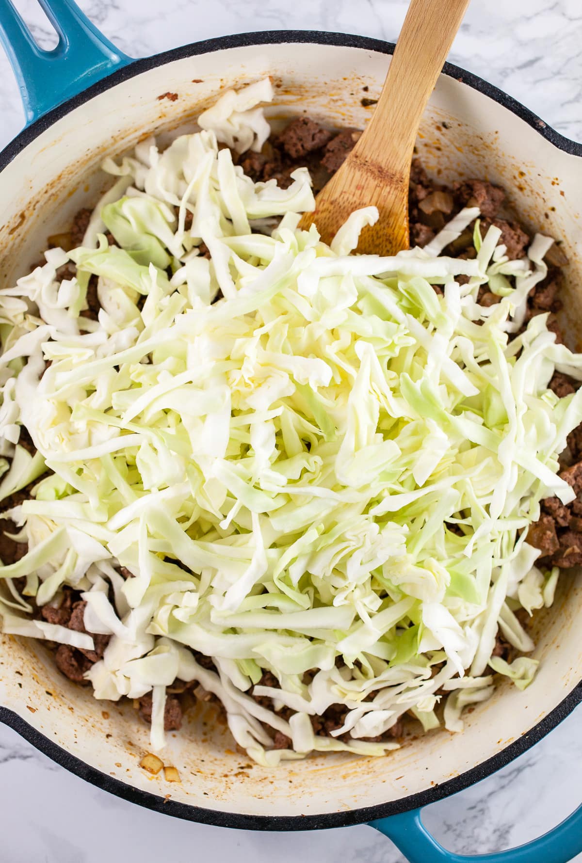 Shredded cabbage added to cooked ground beef mixture in skillet.