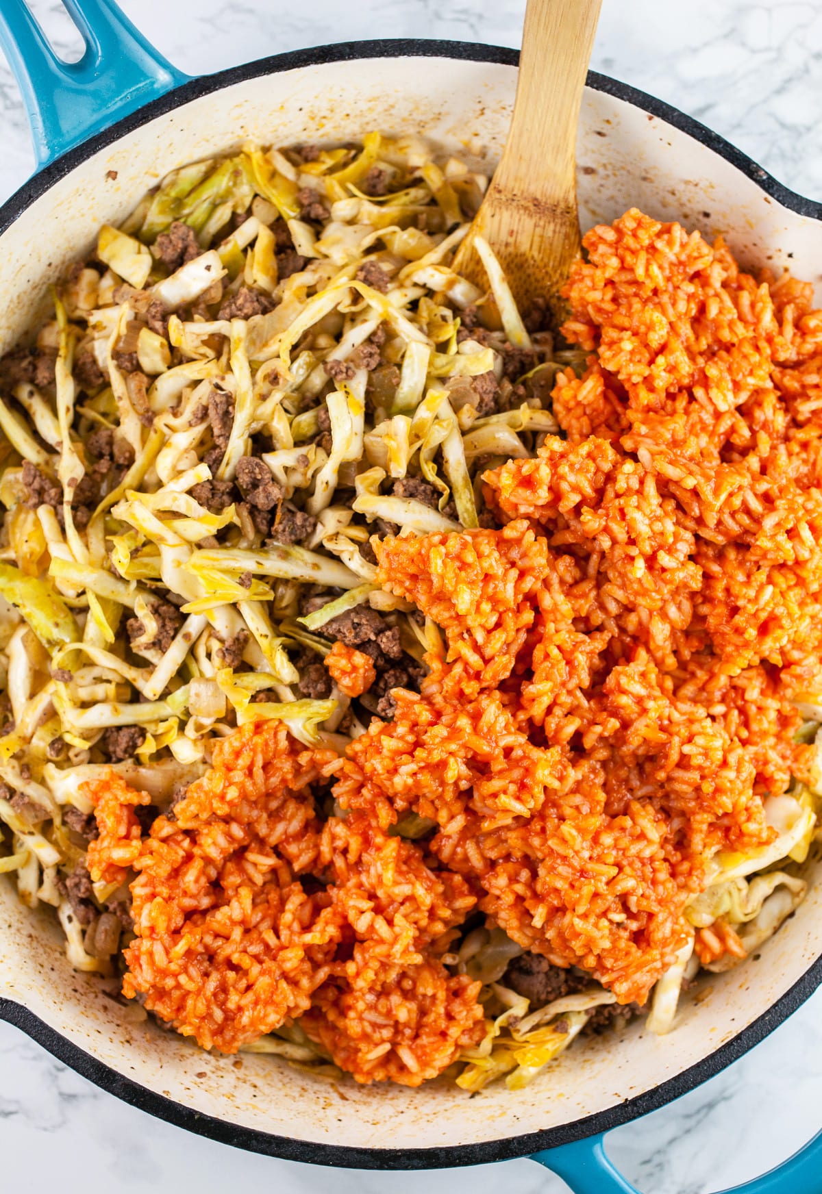 Cooked rice added to ground beef and cabbage in skillet.