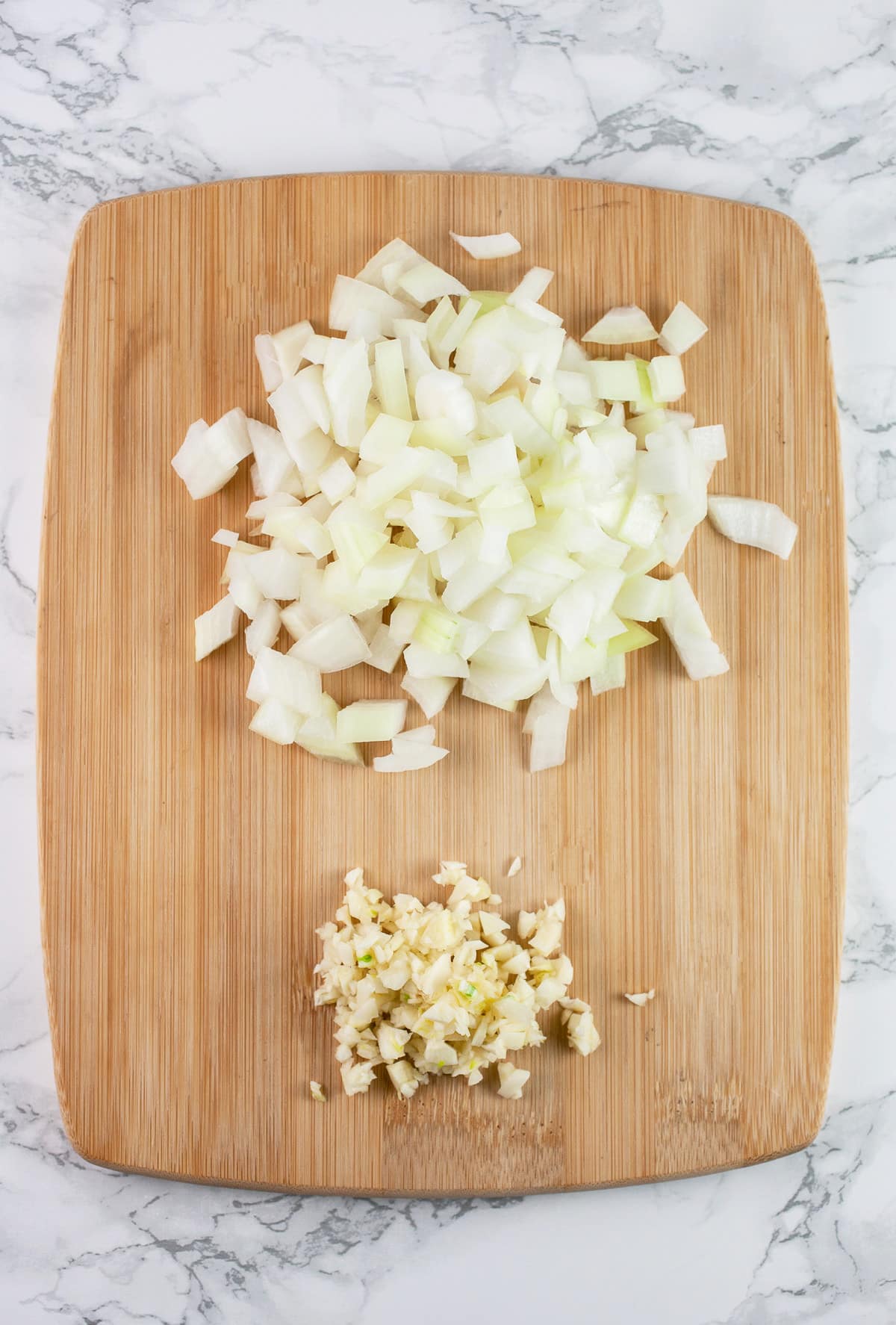Minced garlic and onions on wooden cutting board.