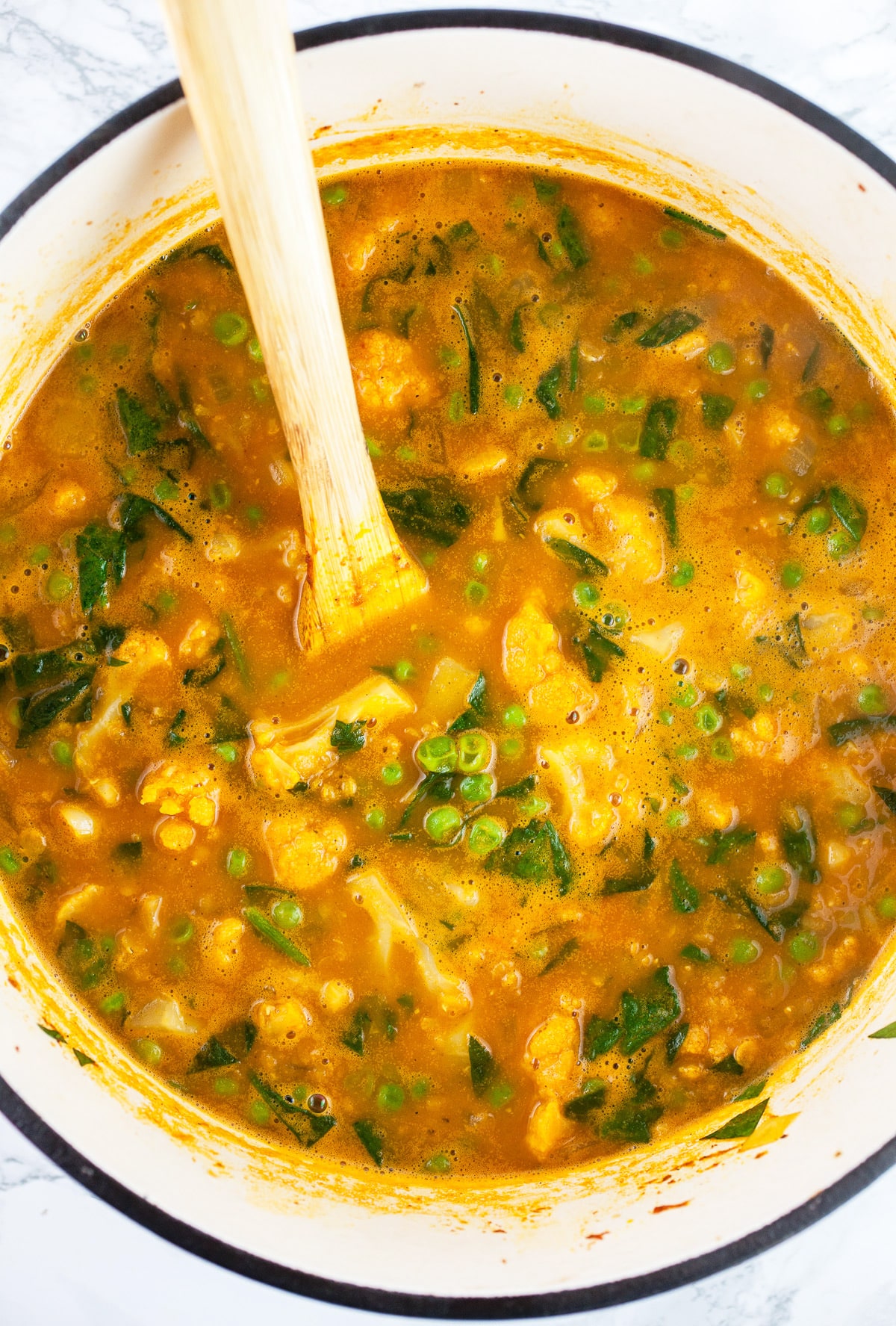 Cooked cauliflower lentil soup in Dutch oven with wooden spoon.