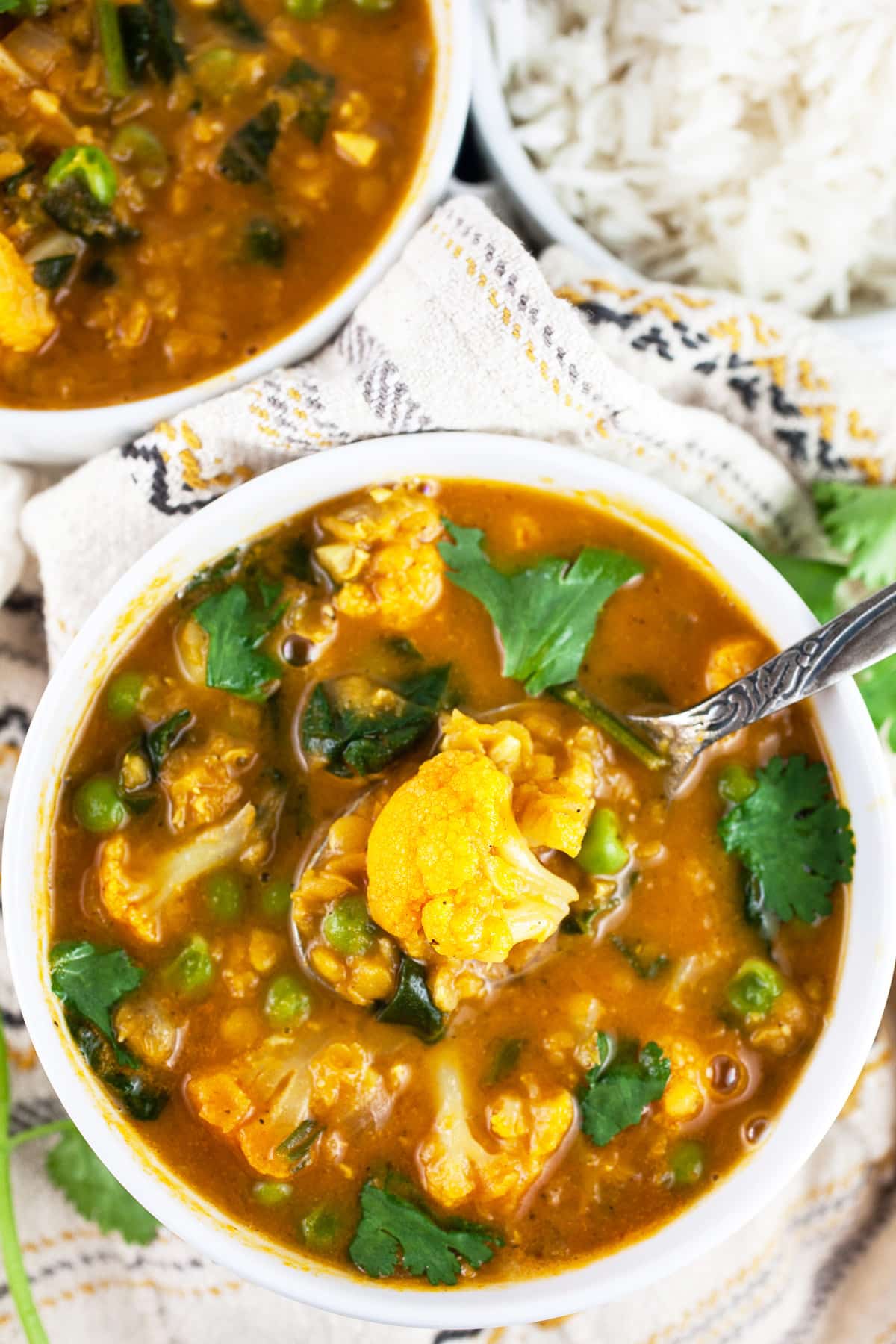 Cauliflower lentil soup with cilantro in white bowl next to Basmati rice.