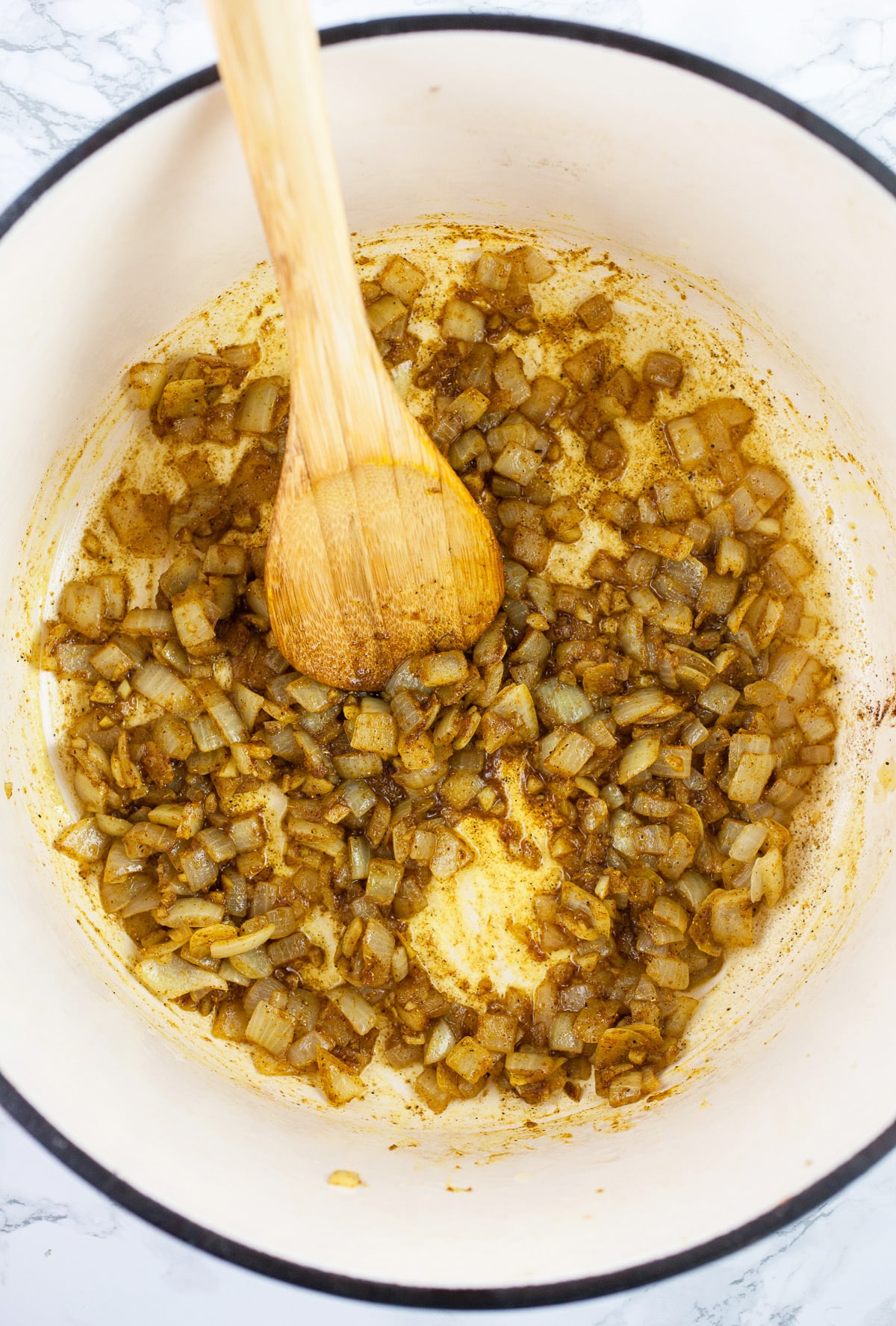 Minced garlic and onions sautéed with spices in Dutch oven with wooden spoon. 