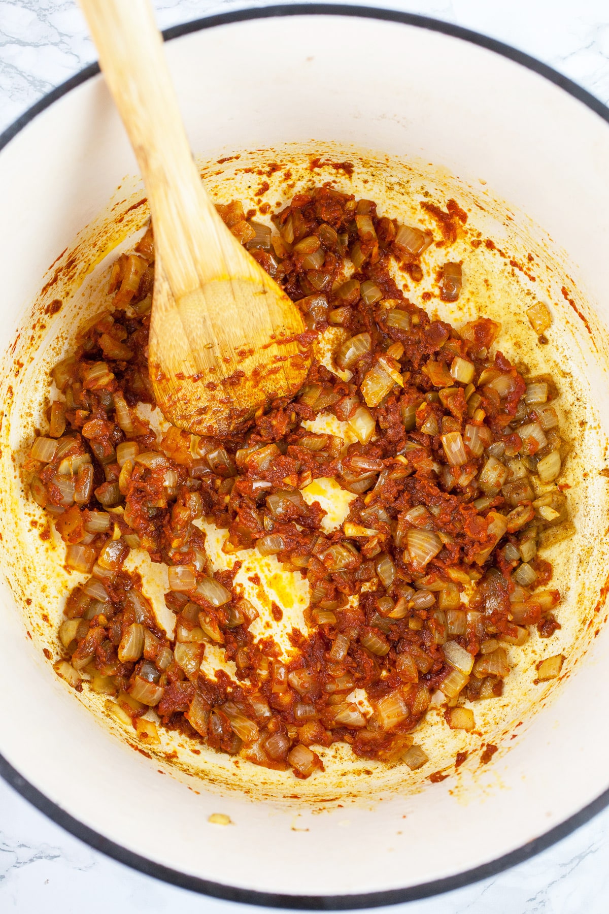 Minced garlic and onions sautéed with spices and tomato paste in Dutch oven with wooden spoon.