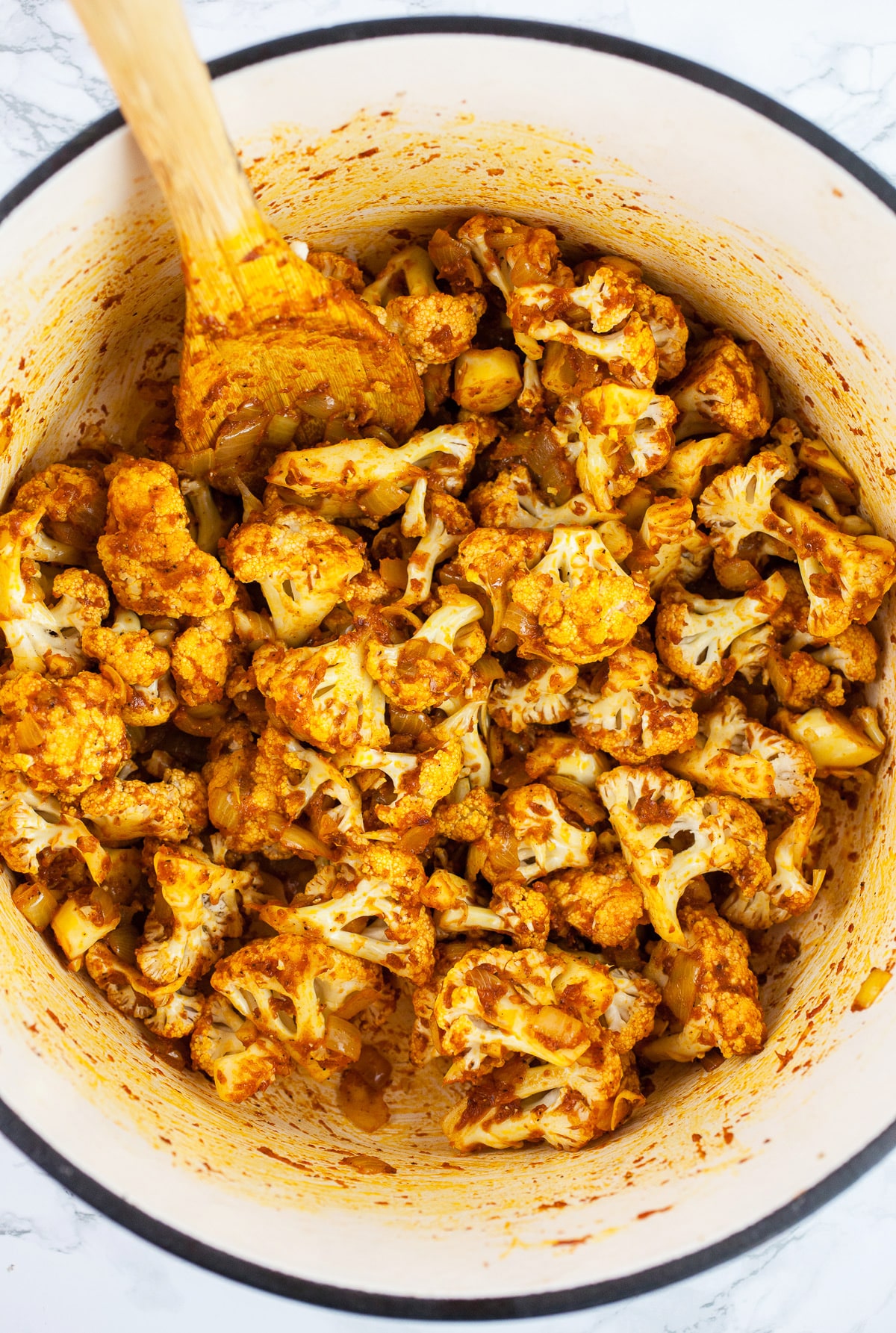 Cauliflower florets sautéed in Dutch oven with spices and tomato paste with wooden spoon.