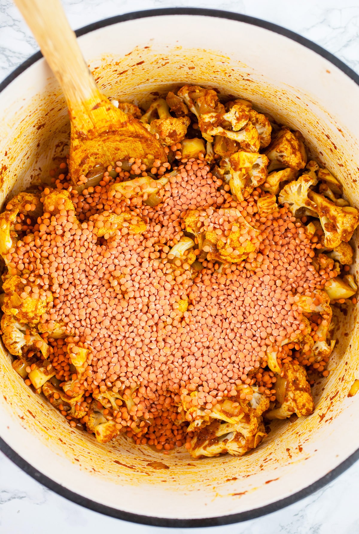 Red lentils and cauliflower with spices in Dutch oven with wooden spoon.