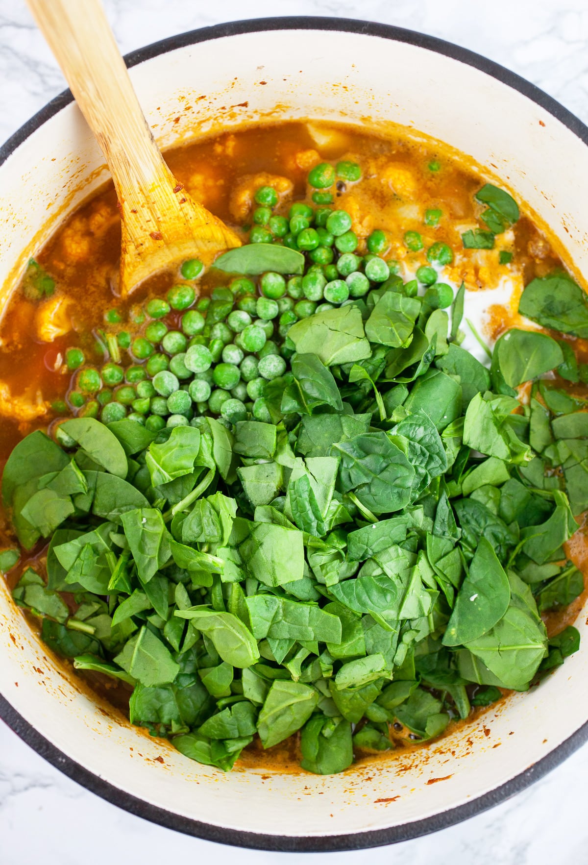 Spinach and peas added to Dutch oven with wooden spoon.