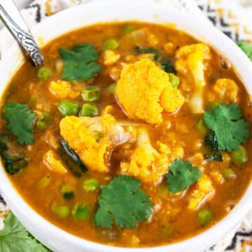 Cauliflower lentil soup with cilantro in white bowl with spoon.