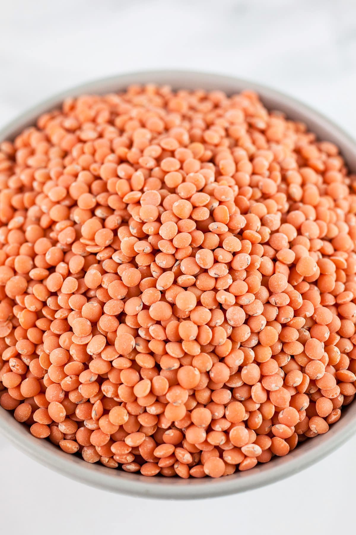 Uncooked red lentils in small grey bowl.