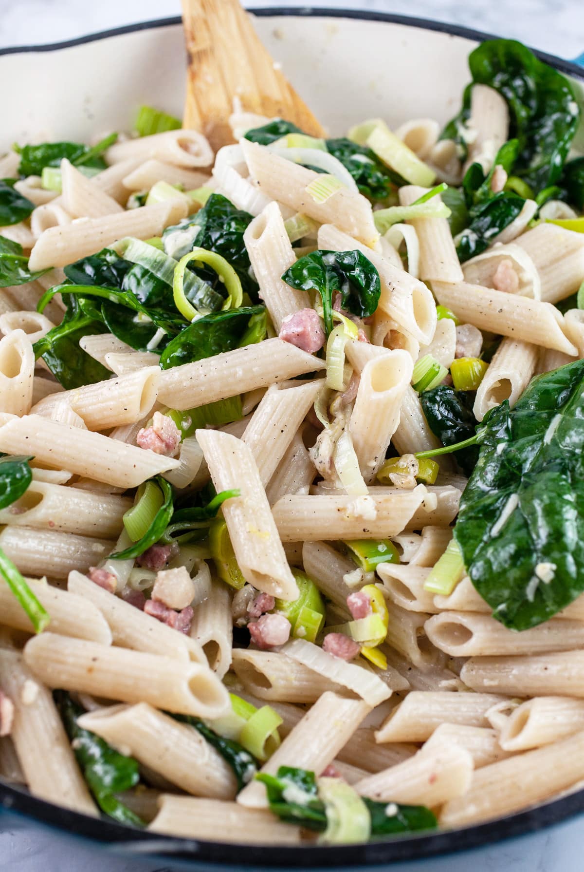 Leek pancetta pasta in skillet with wooden spoon.