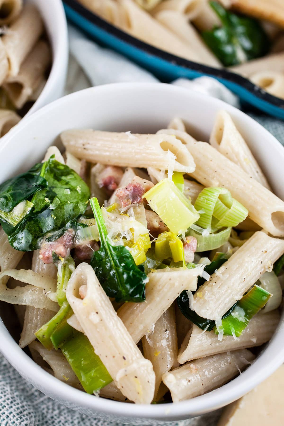 Leek pancetta pasta in white bowls next to skillet.