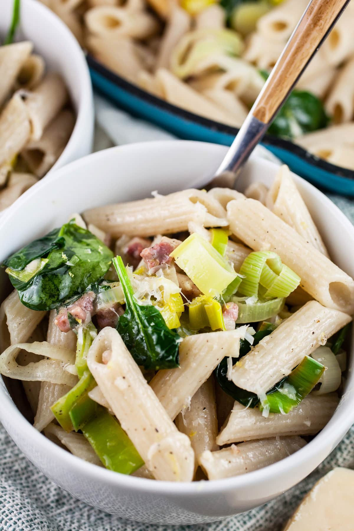 Leek pancetta pasta in white bowl with fork next to skillet.