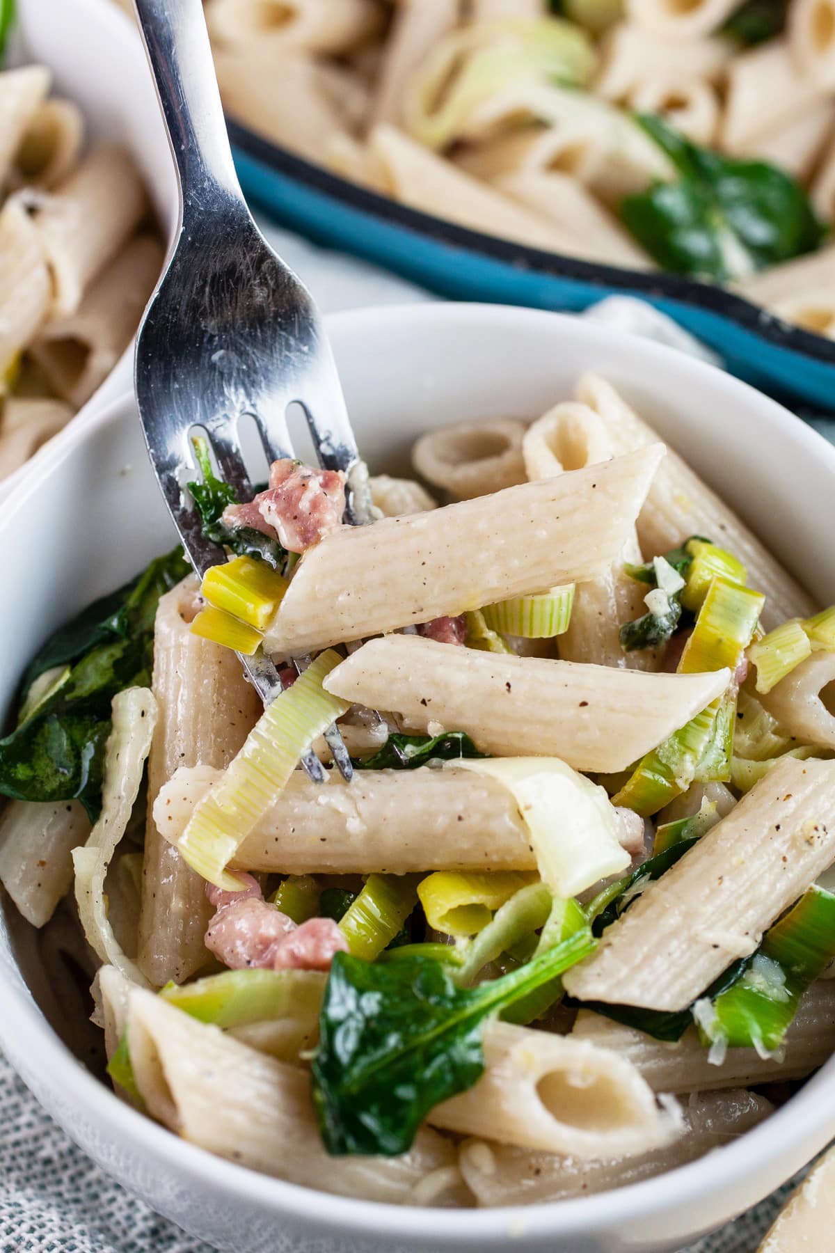 Forkful of leek pancetta pasta lifted from white bowl.