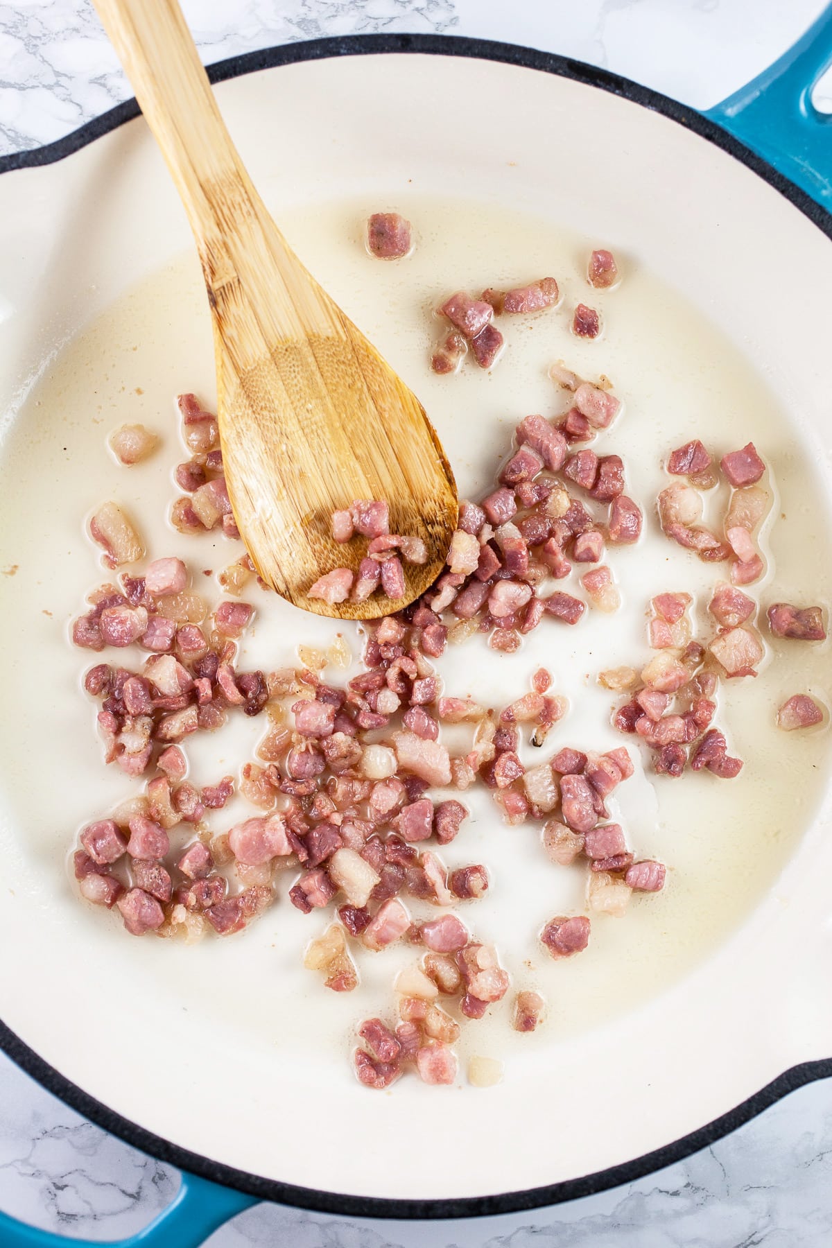 Diced pancetta sautéed in skillet with wooden spoon. 