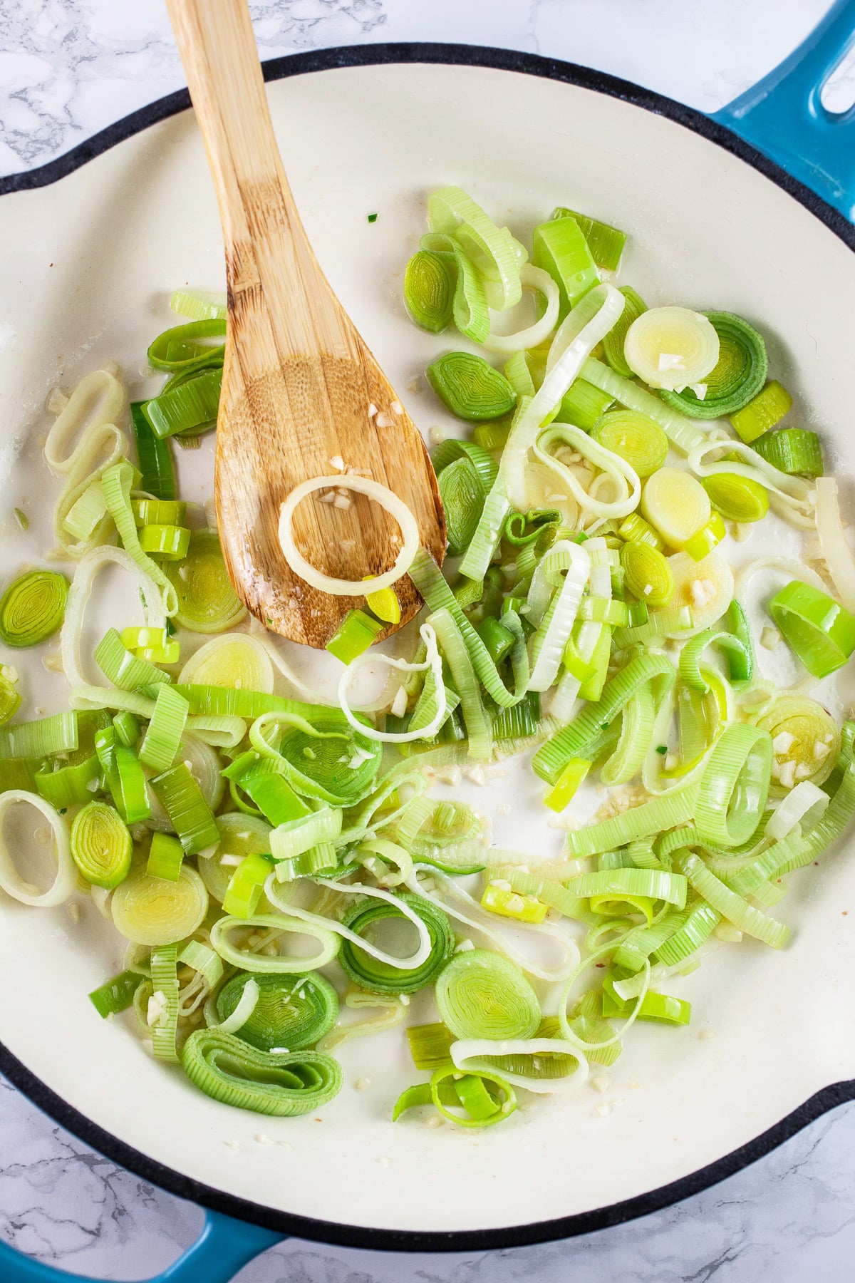 Sliced leeks sautéed in skillet with wooden spoon.