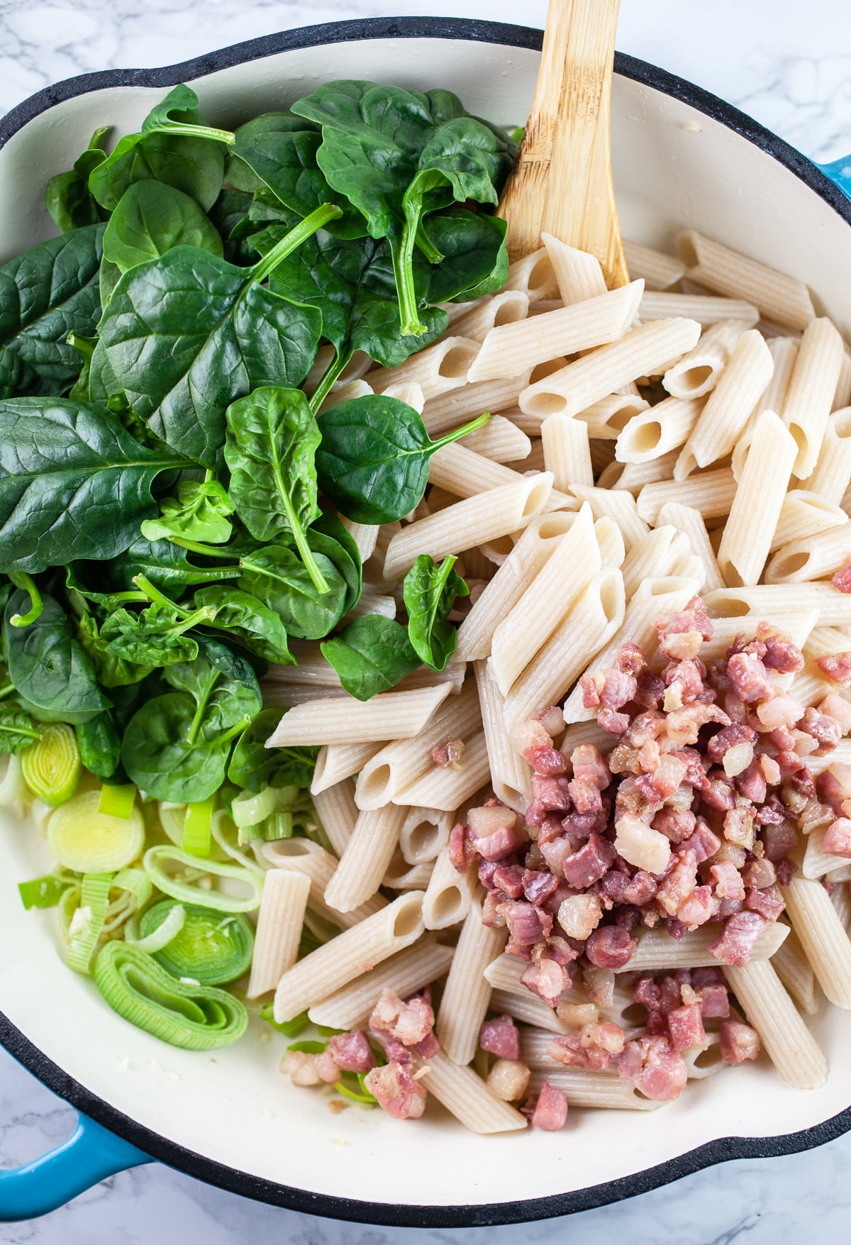 Cooked pasta, pancetta, leeks, and spinach in skillet with wooden spoon.