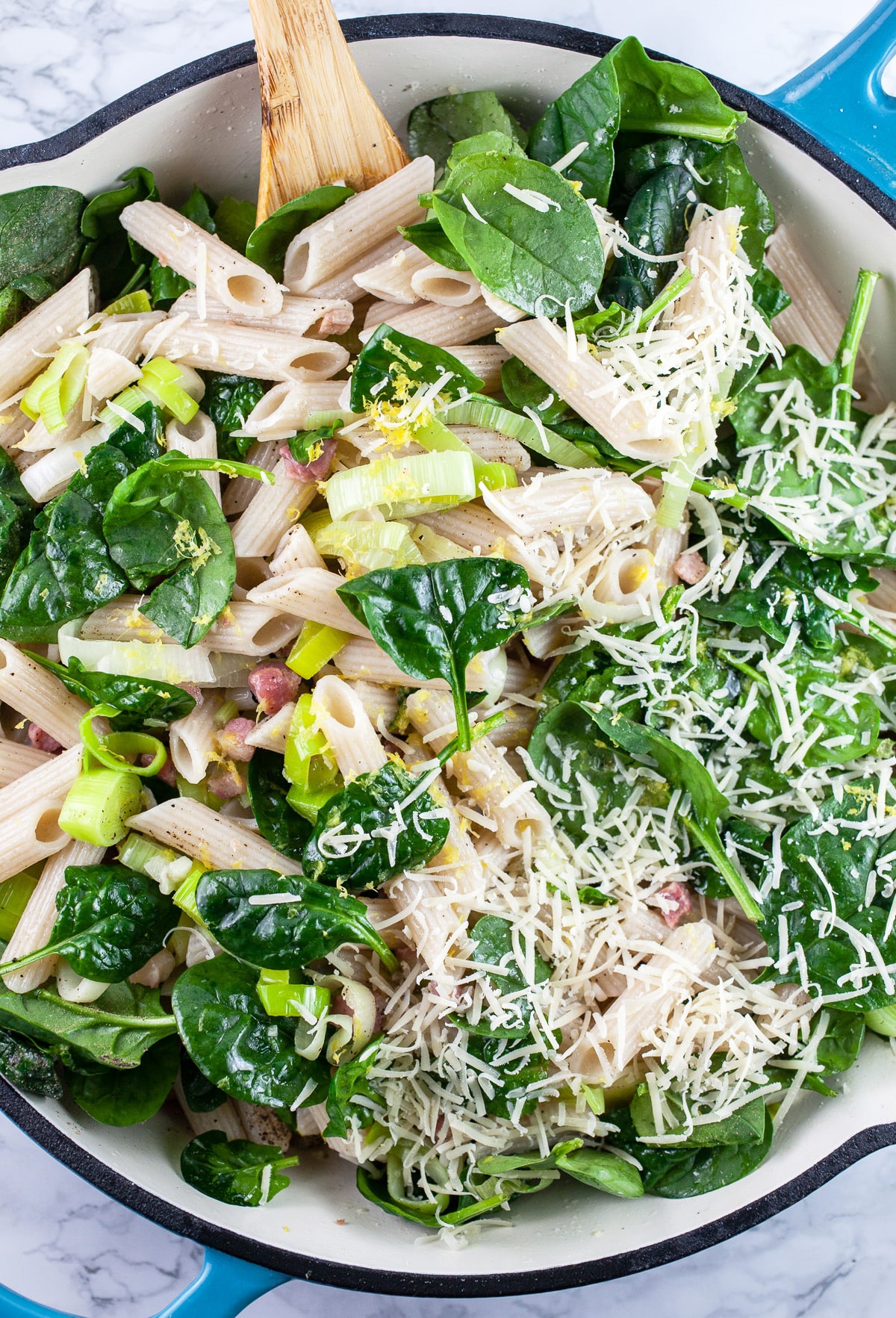 Pancetta leek pasta with spinach in skillet with wooden spoon.