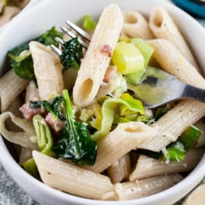 Leek pancetta pasta in white bowl with fork.