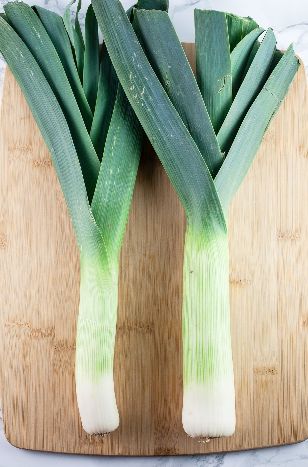 Whole leeks on wooden cutting board.