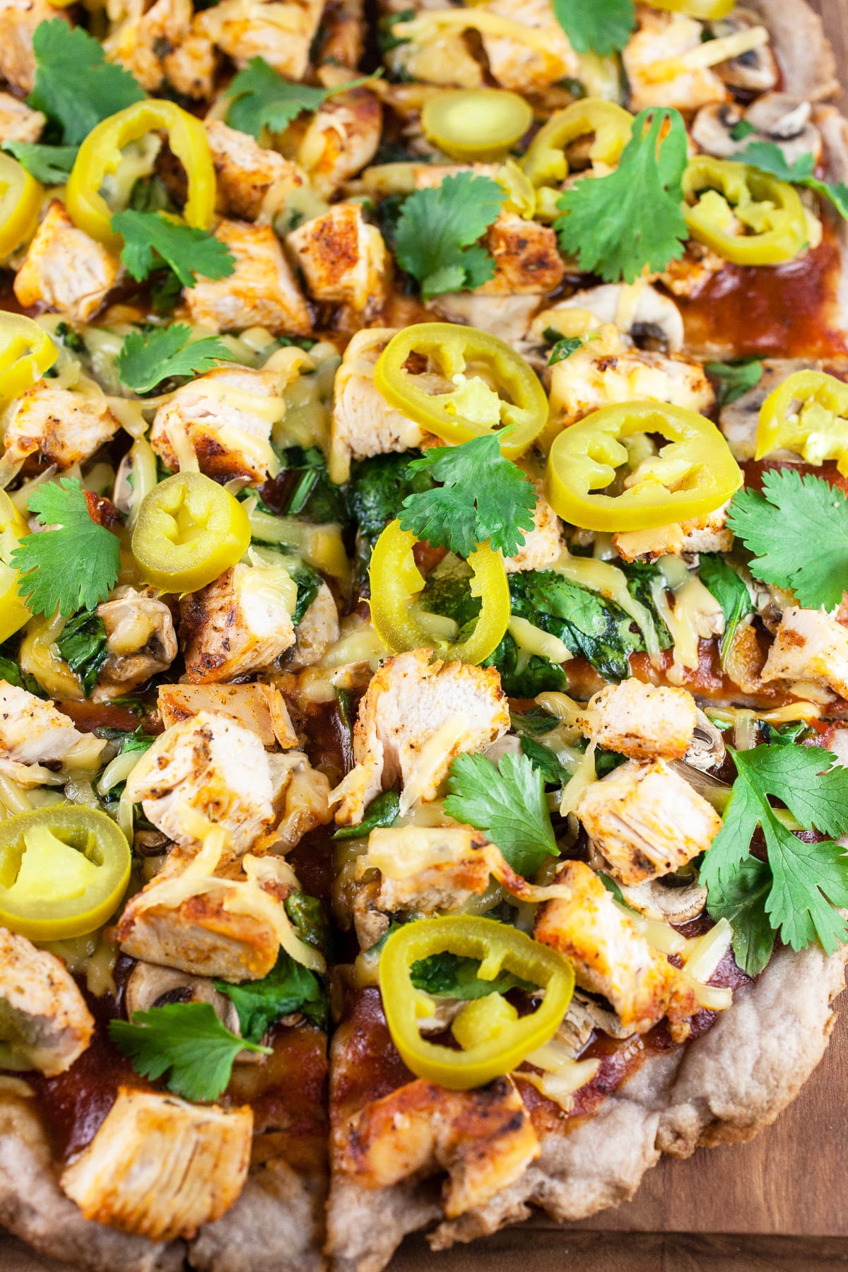 BBQ chicken pizza cut into slices on wooden cutting board.