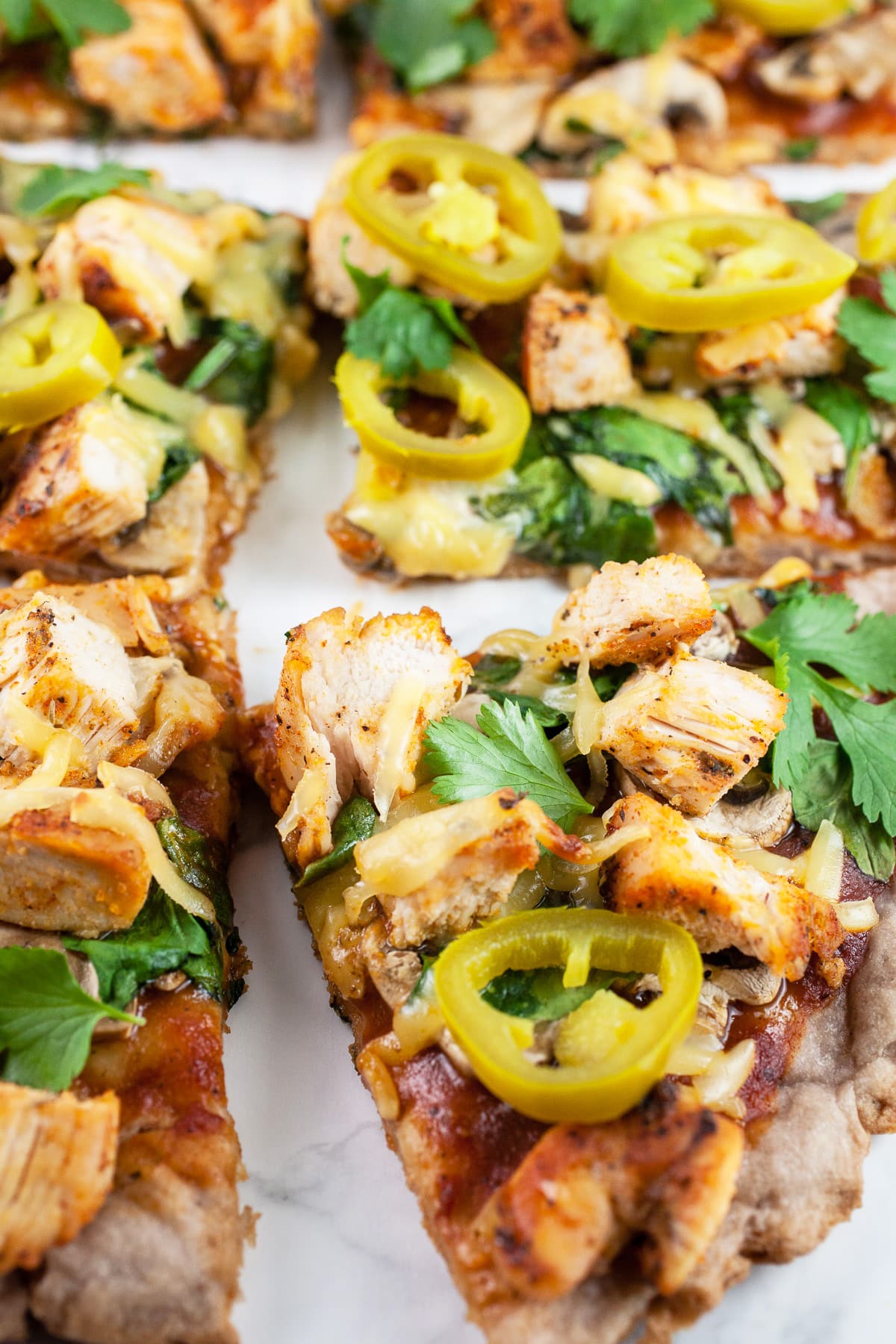 This Smoky BBQ Chicken Pizza recipe is homemade, easy to make, and healthy! It's got a scratch-made pizza crust and is topped with spicy chicken, barbecue sauce, Gouda cheese, spinach, and cilantro. This makes great simple meals for families or awesome fun appetizers for parties like the Super Bowl. It's one of the best pizzas out there! #bbqchicken #pizza #recipes #bbq #chicken #Gouda #homemade BBQ chicken pizza with pickled jalapenos cut into slices.