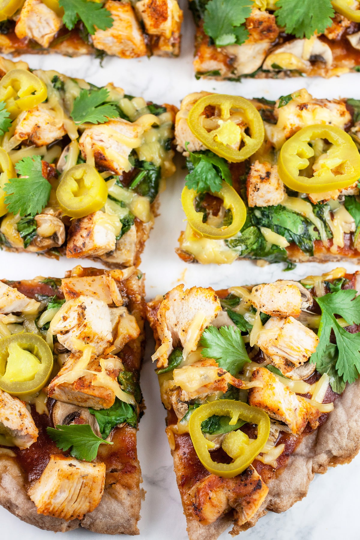 BBQ chicken pizza cut into slices on white surface.