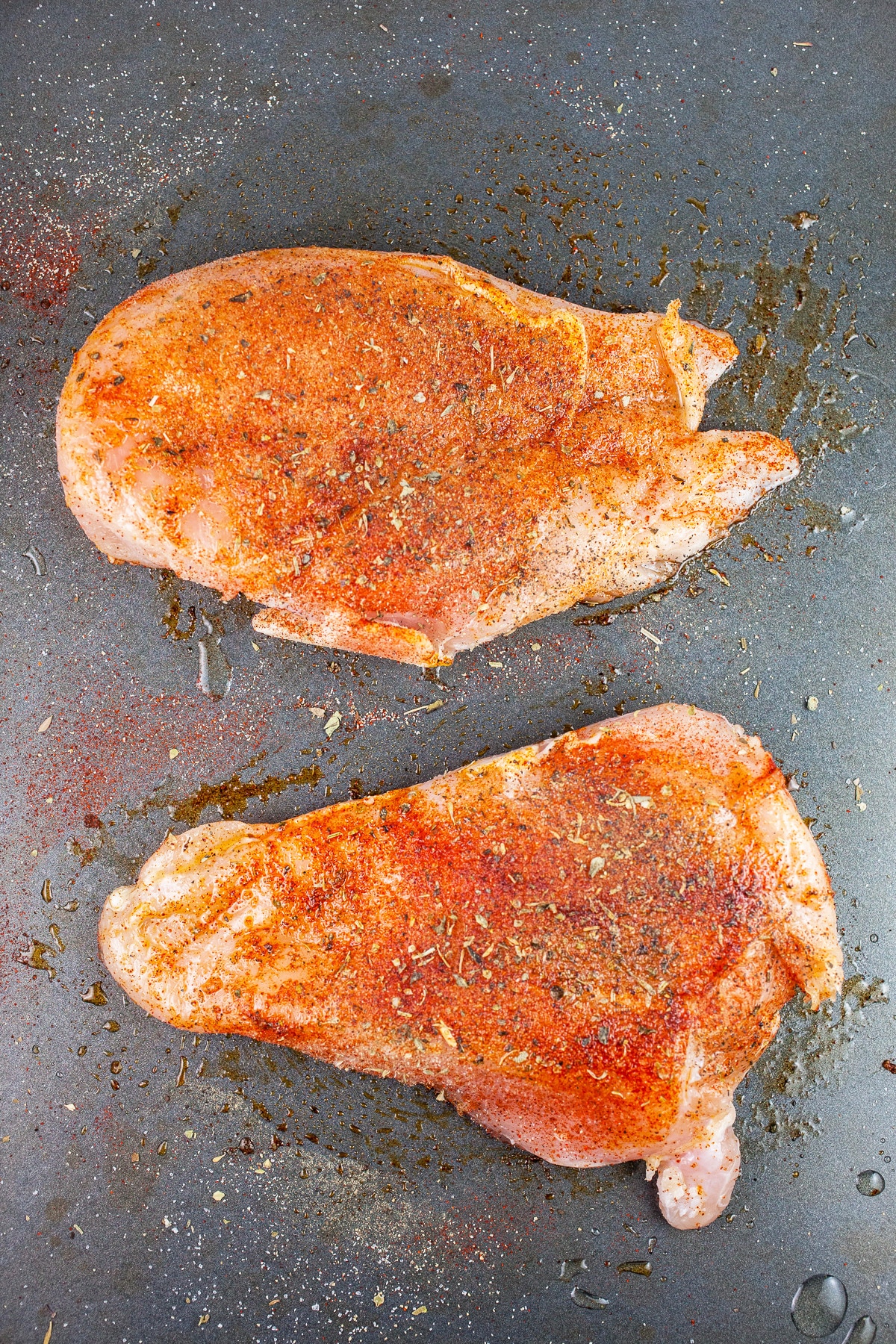Uncooked spiced chicken breasts on baking sheet.