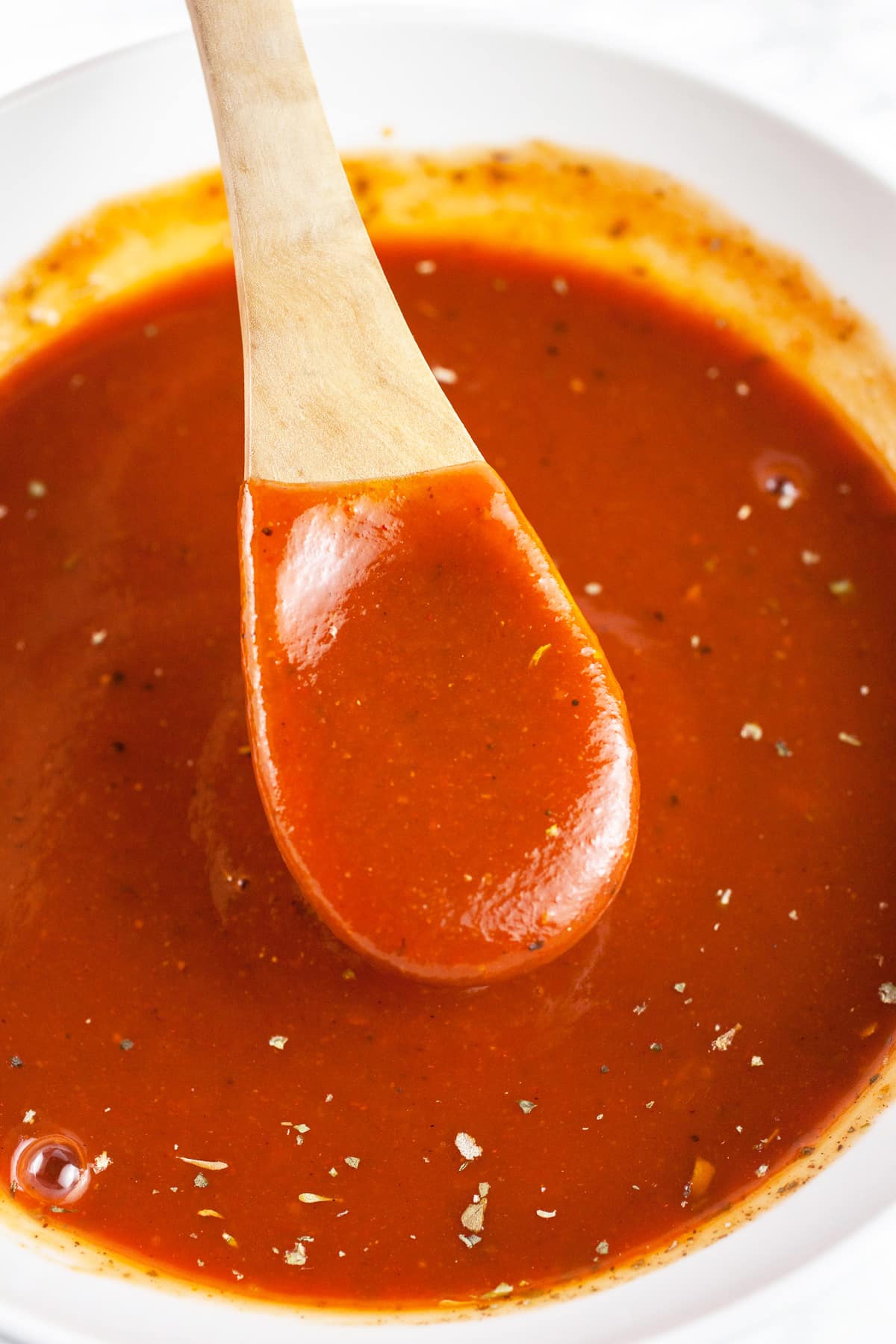 Wooden spoonful of BBQ sauce mixture lifted from white bowl.