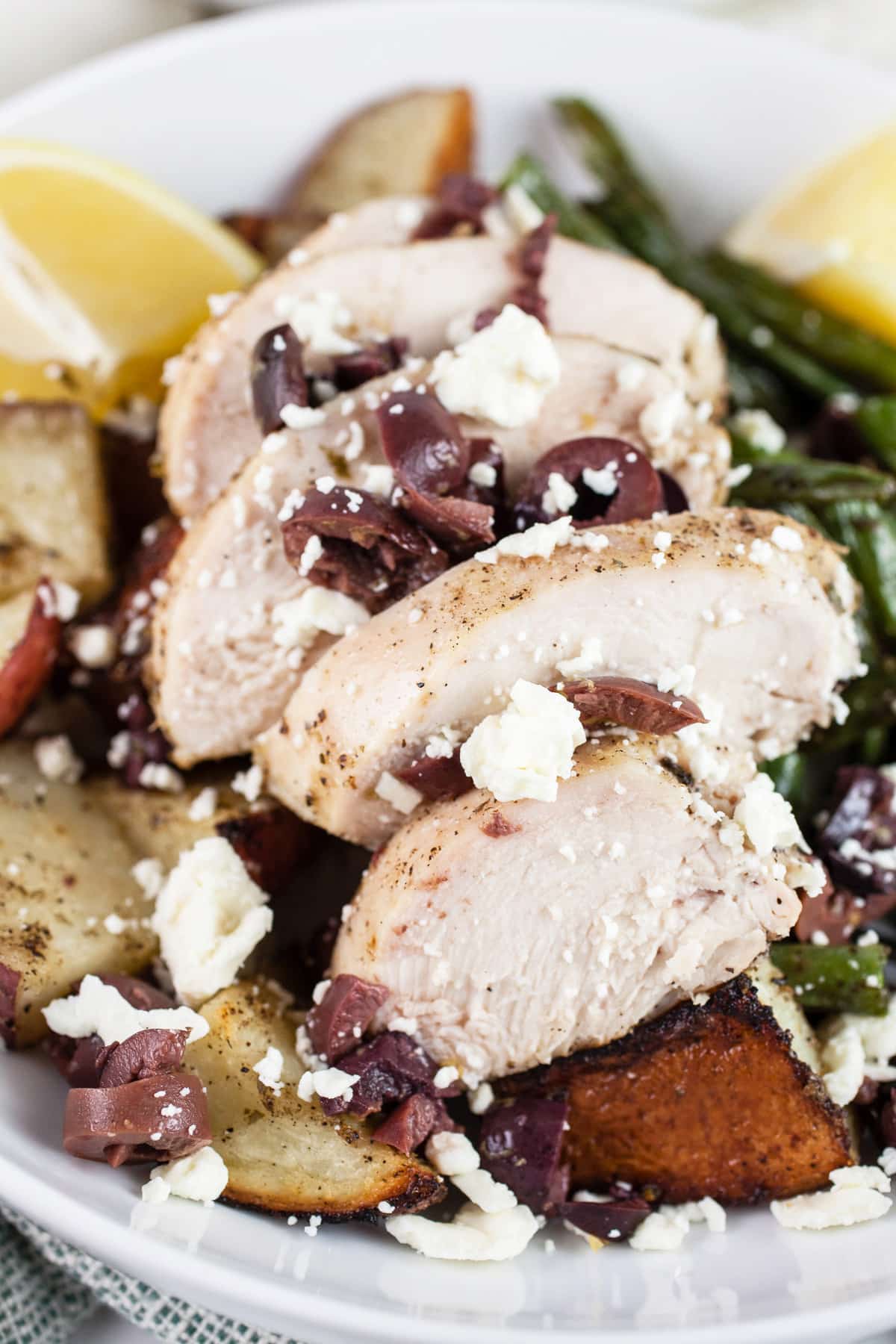 Sheet pan Greek chicken with potatoes, green beans, feta, and Kalamata olives in white bowl.